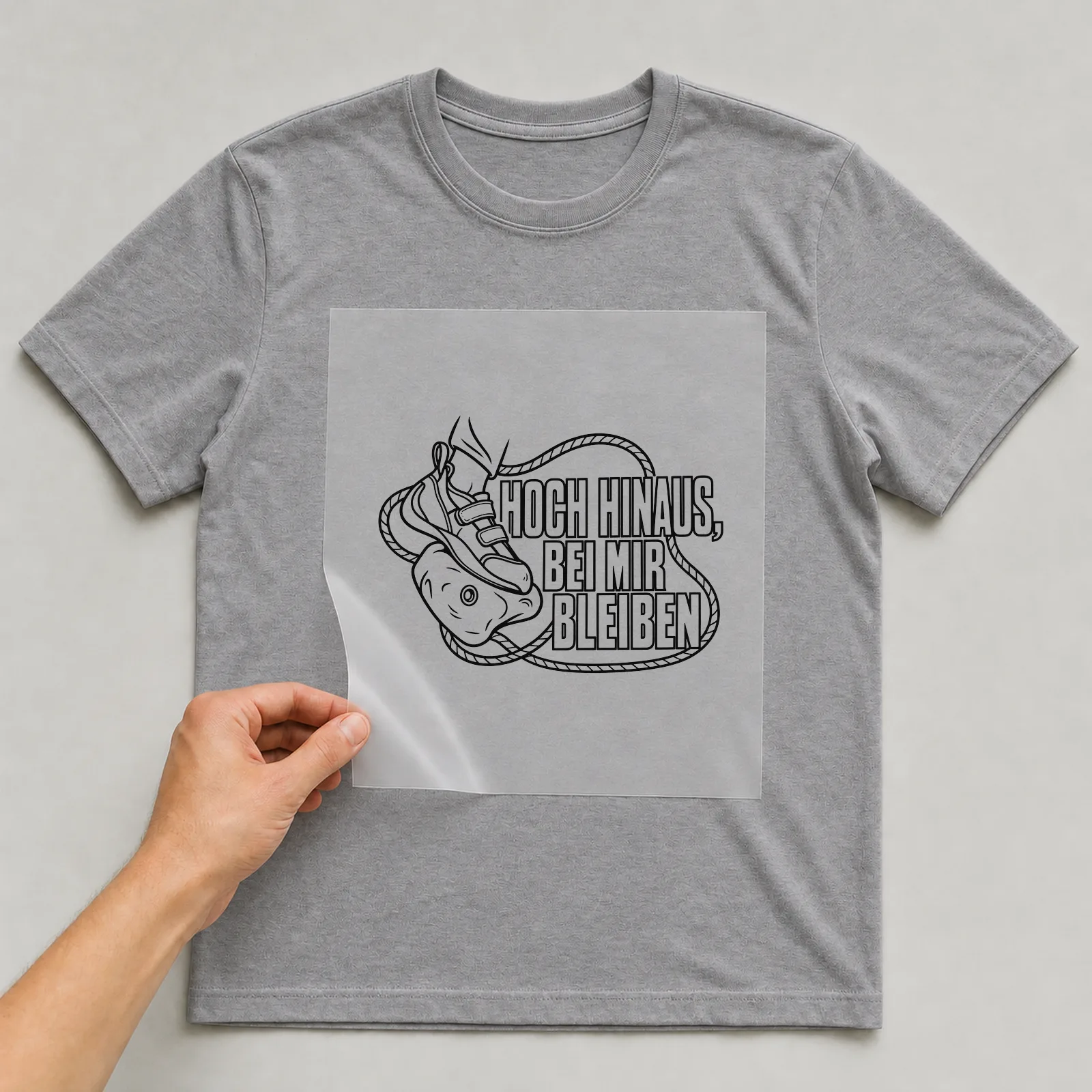 Bügelbild „Hoch hinaus, bei mir bleiben“ auf grauem T-Shirt, Folie wird aufgelegt