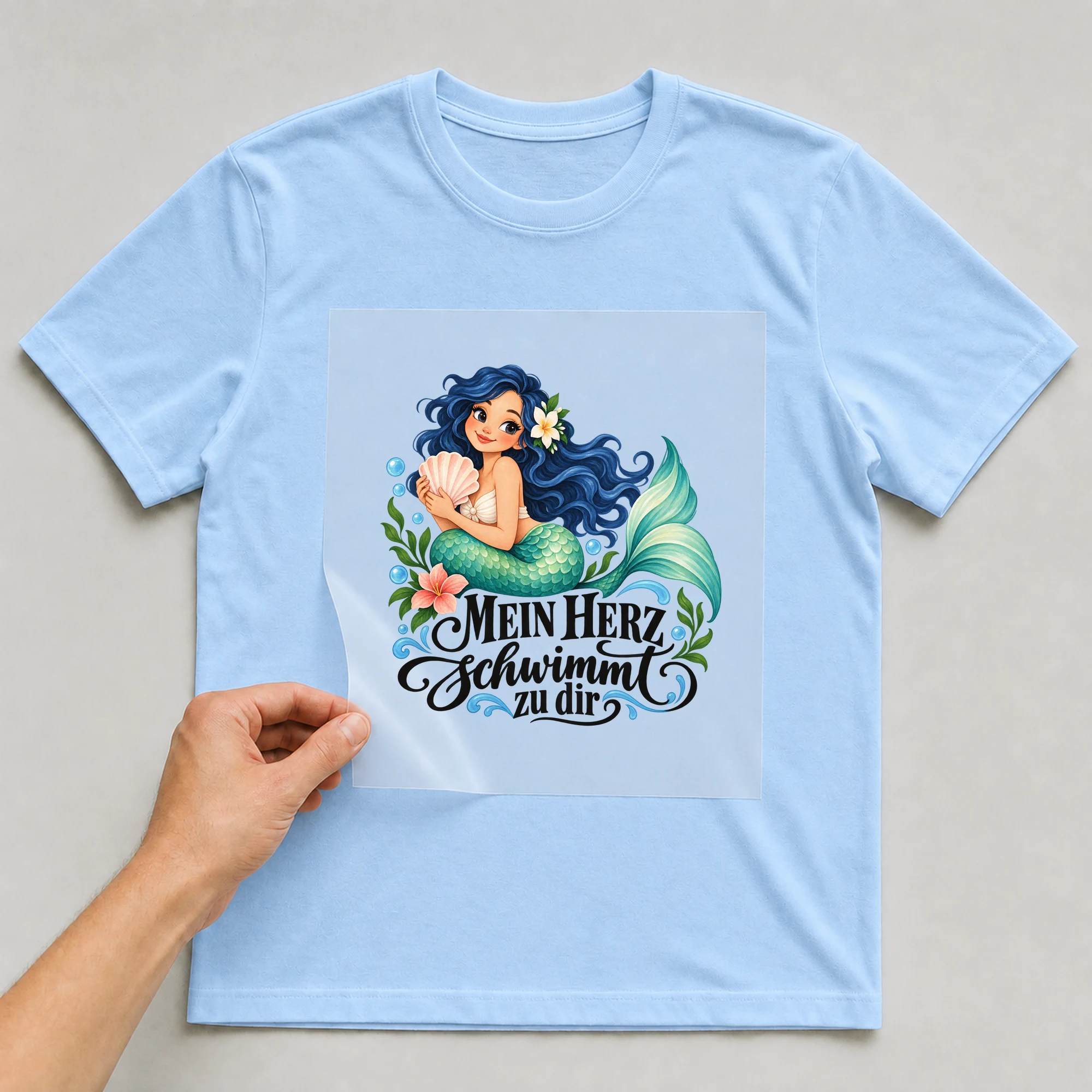 Bügelbild „Mein Herz schwimmt zu dir“ auf babyblauem T-Shirt, Folie wird aufgelegt