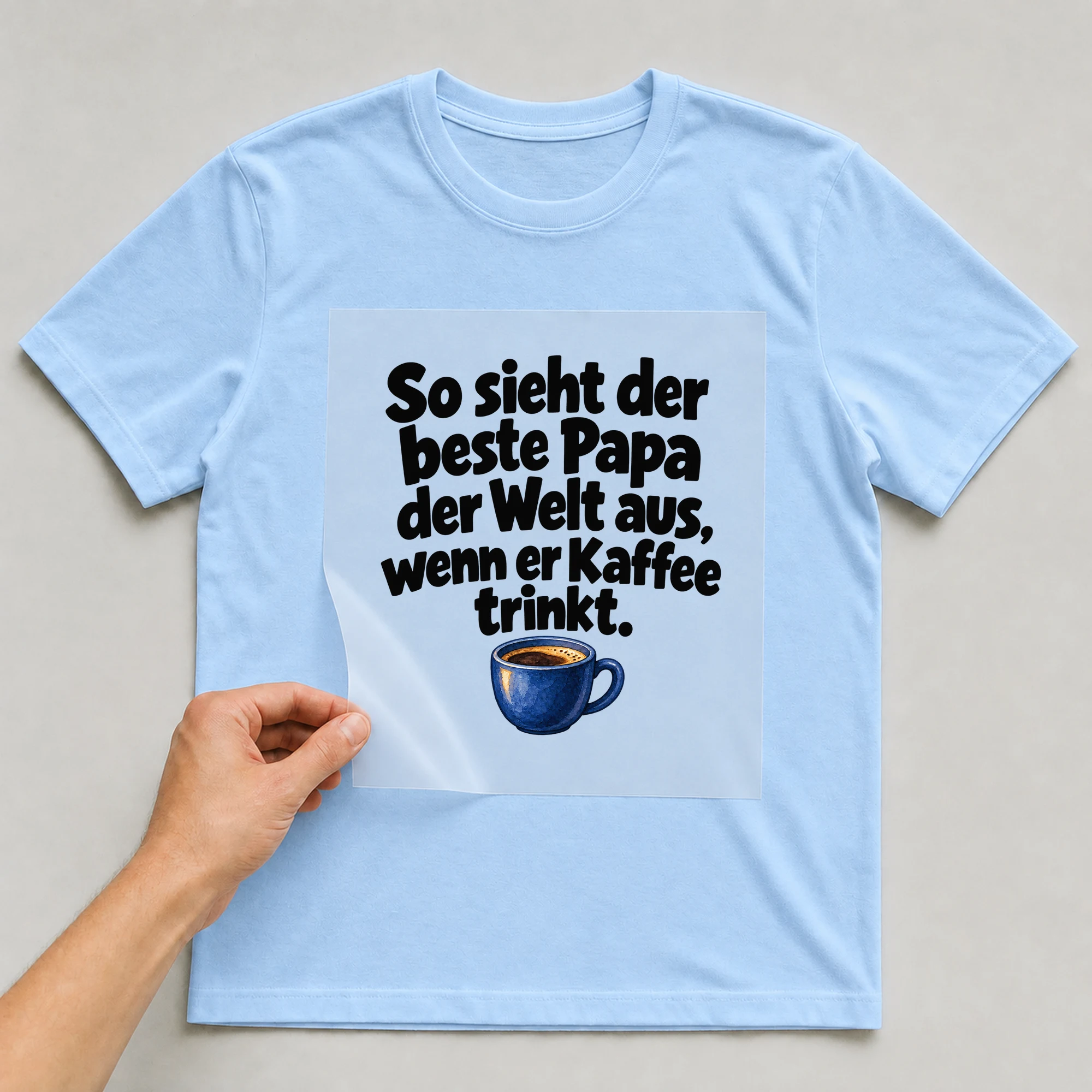 Bügelbild „So sieht der beste Papa der Welt aus, wenn er Kaffee trinkt.“ auf babyblauem T-Shirt, Folie wird aufgelegt
