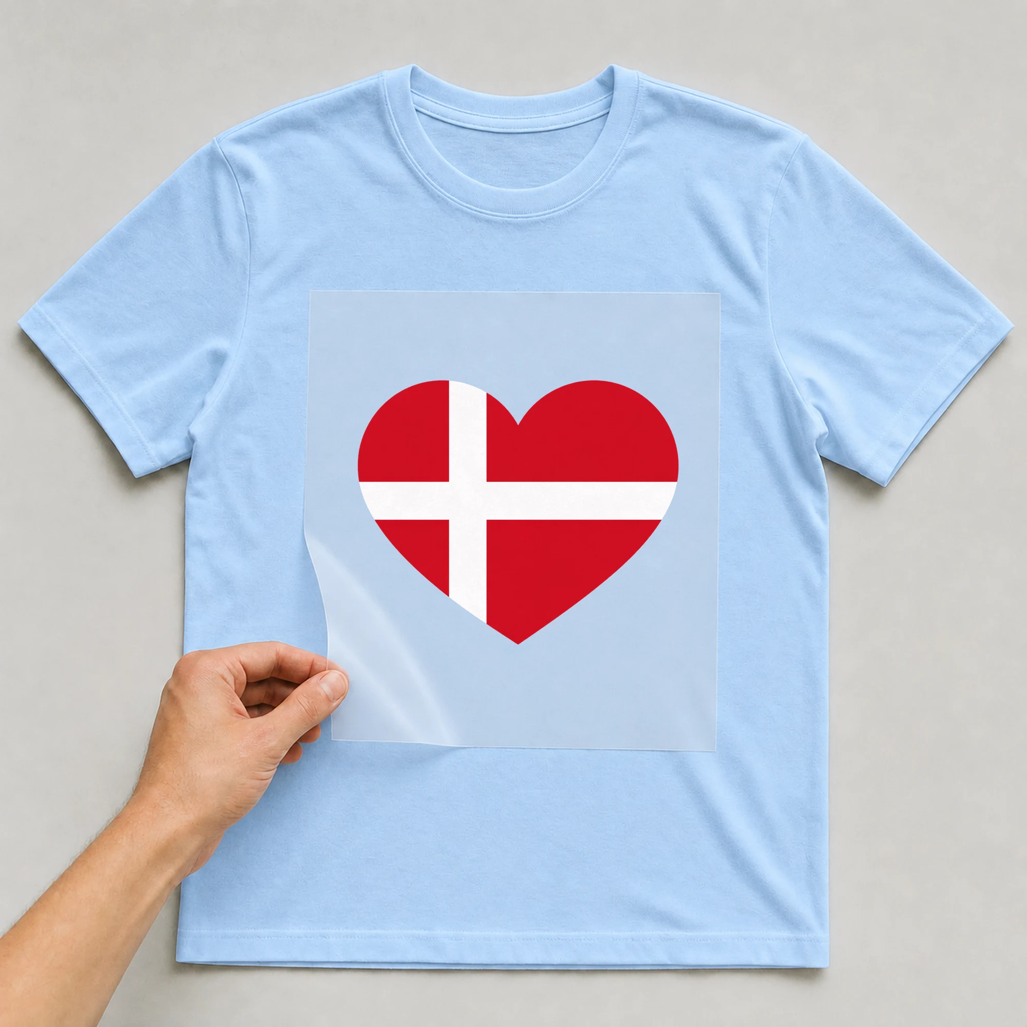 Bügelbild „Länder Flagge Dänemark“ auf babyblauem T-Shirt, Folie wird aufgelegt