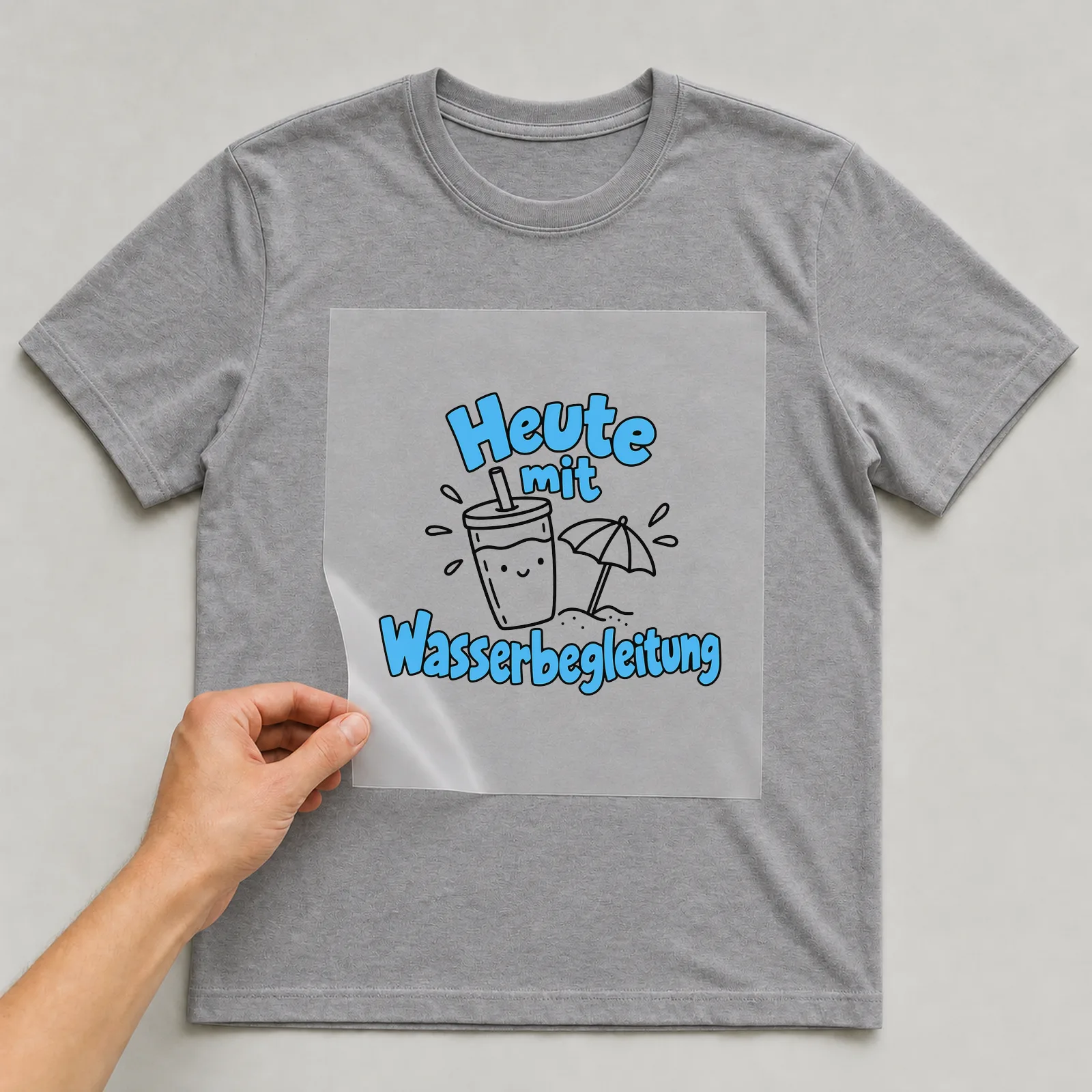Bügelbild „Heute mit Wasserbegleitung“ auf grauem T-Shirt, Folie wird aufgelegt