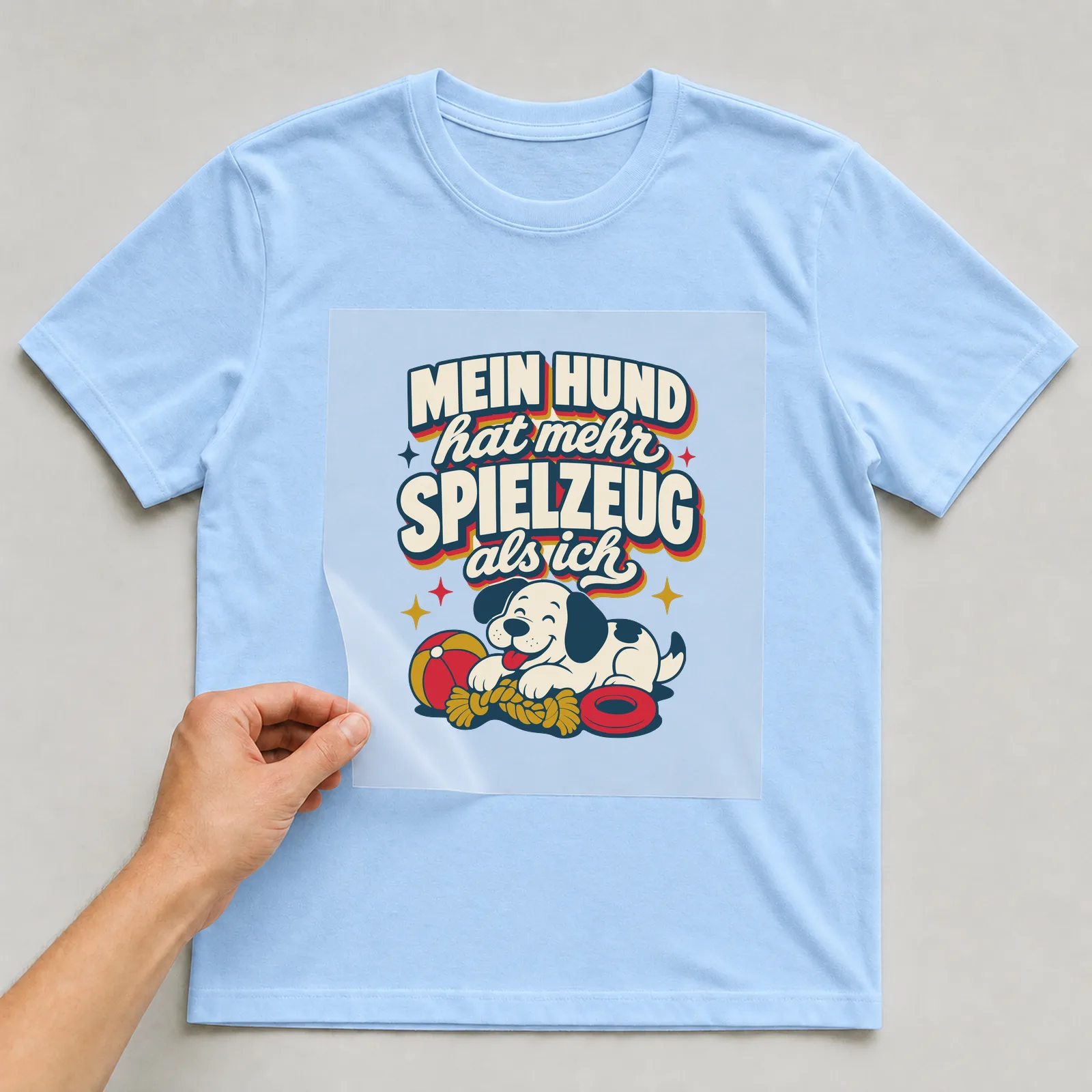 Bügelbild Mein Hund hat mehr Spielzeug als ich auf hellblauem T-Shirt, Folie wird aufgelegt