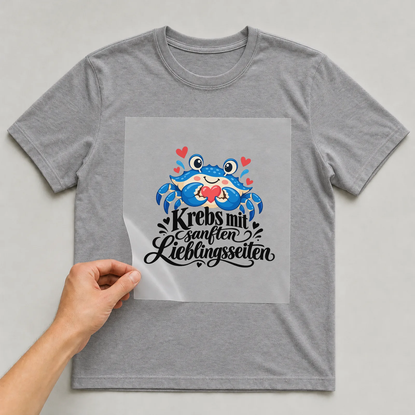 Bügelbild „Krebs mit sanften Lieblingsseiten“ auf grauem T-Shirt, Folie wird aufgelegt