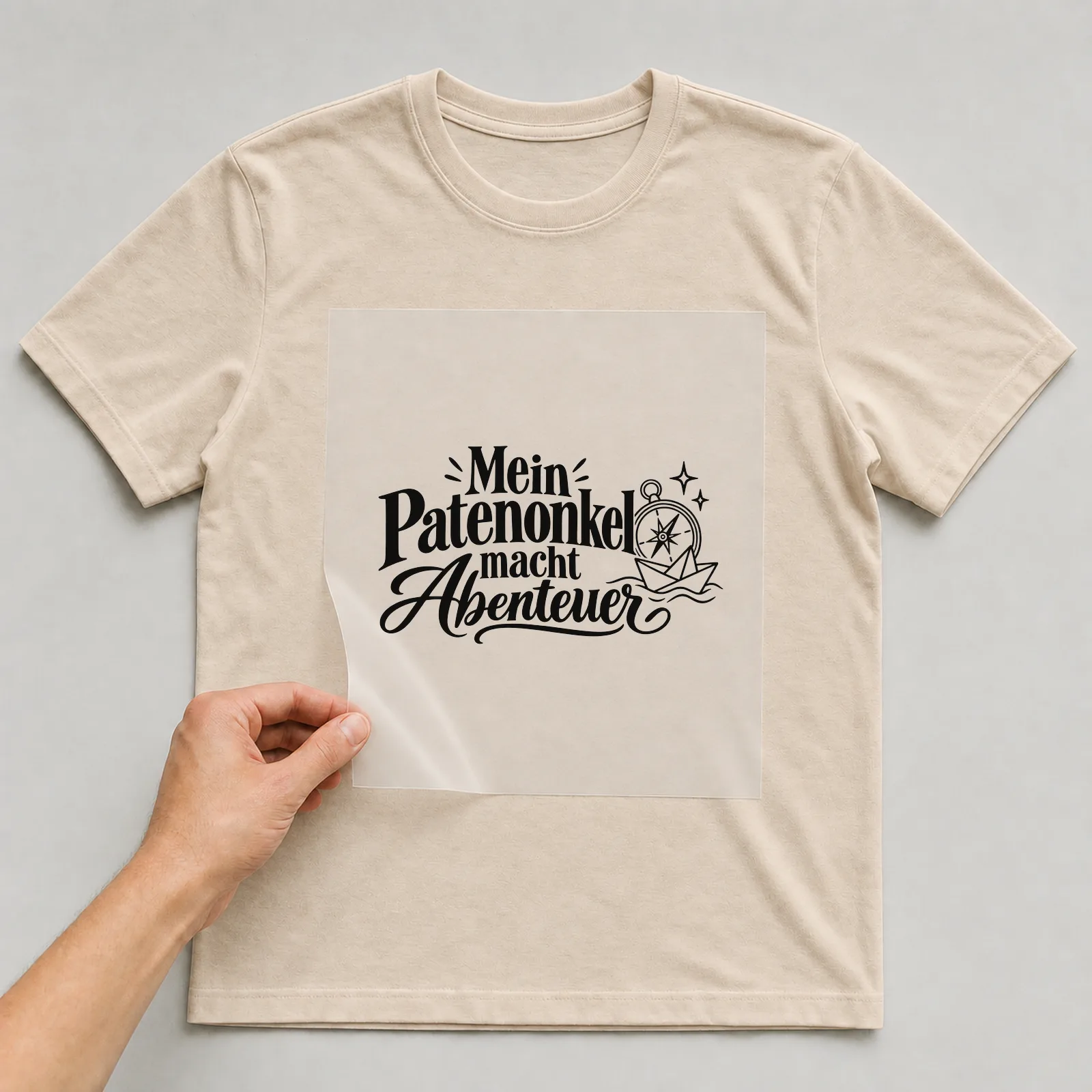 Bügelbild „Mein Patenonkel macht Abenteuer“ auf beigem T-Shirt, Folie wird aufgelegt
