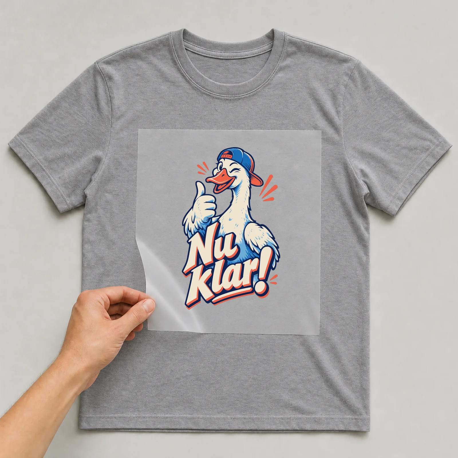 Bügelbild Nu klar! auf grauem T-Shirt, Folie wird aufgelegt