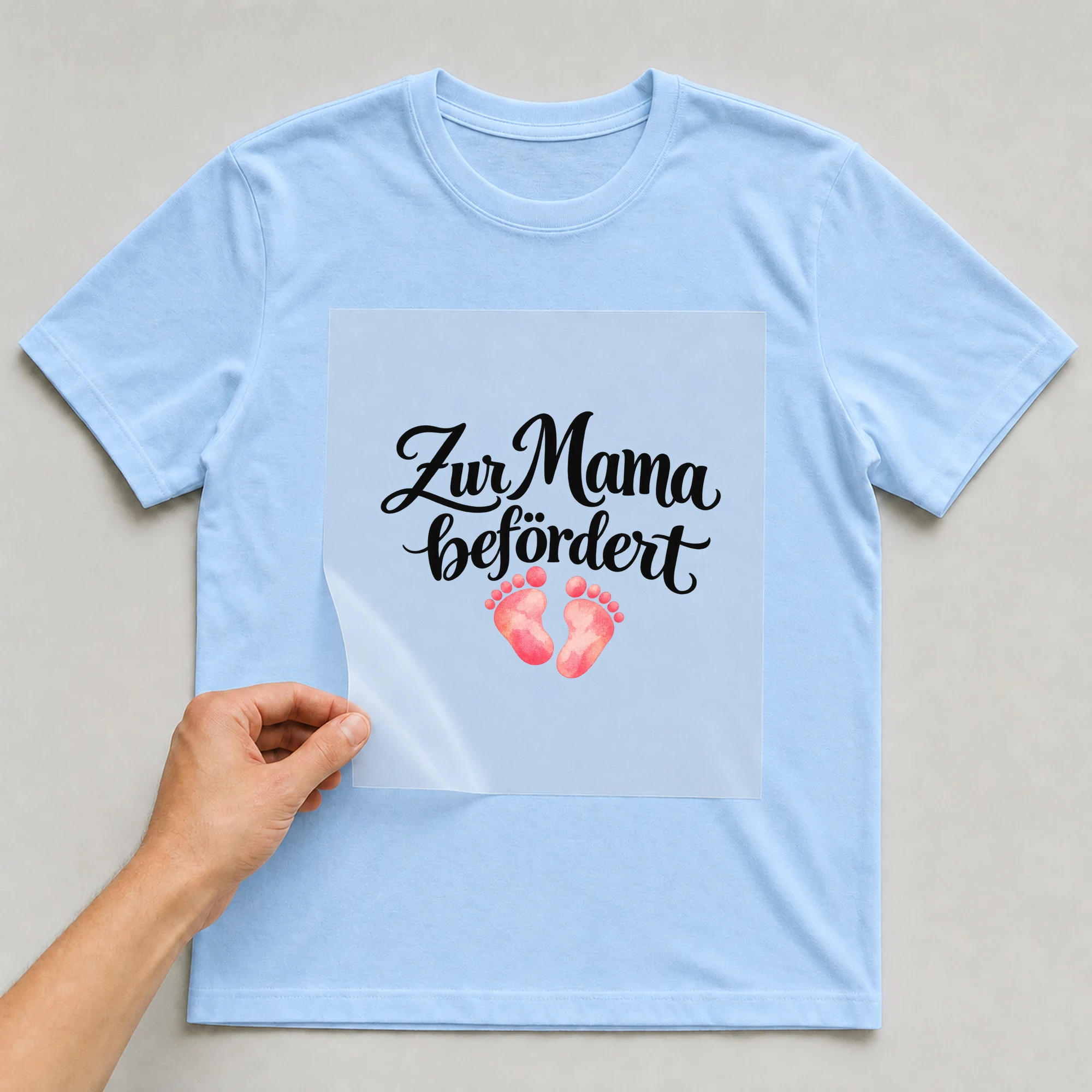 Bügelbild „Zur Mama befördert“ auf babyblauem T-Shirt, Folie wird aufgelegt