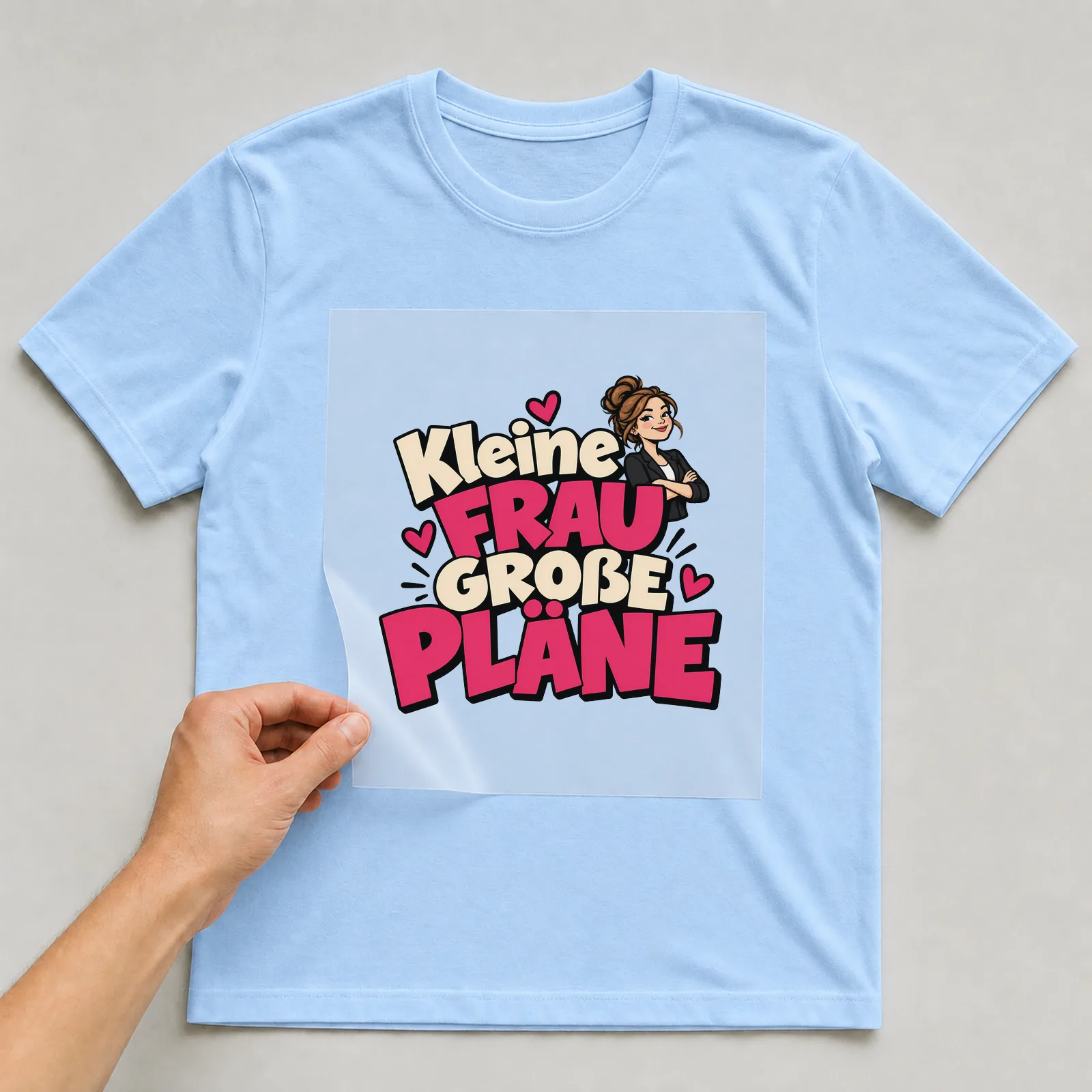 Bügelbild „Kleine Frau große Pläne“ auf hellblauem T-Shirt, Folie wird aufgelegt