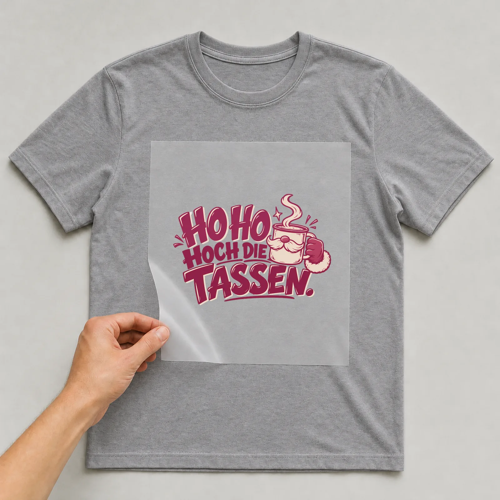 Bügelbild „Ho Ho hoch die Tassen“ auf grauem T-Shirt, Folie wird aufgelegt