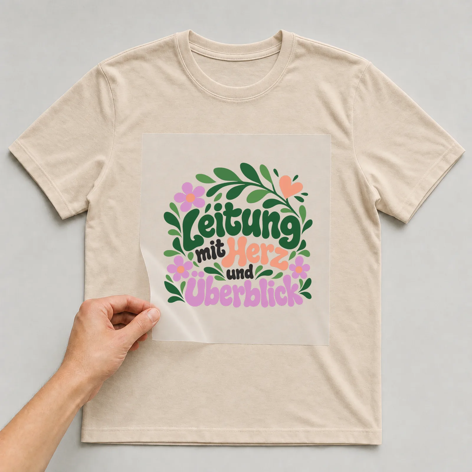 Bügelbild „Leitung mit Herz und Überblick“ auf beigem T-Shirt, Folie wird aufgelegt