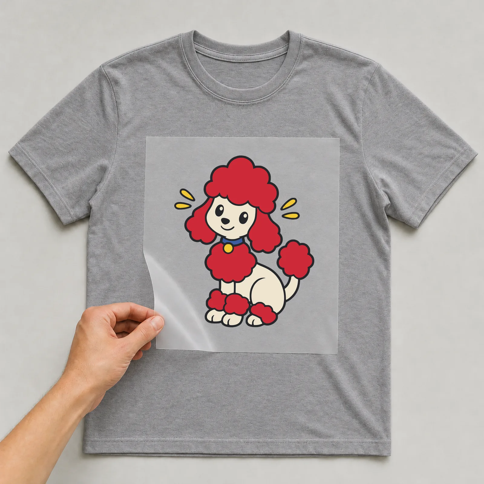 Bügelbild Pudel im Comic-Stil auf grauem T-Shirt, Folie wird aufgelegt