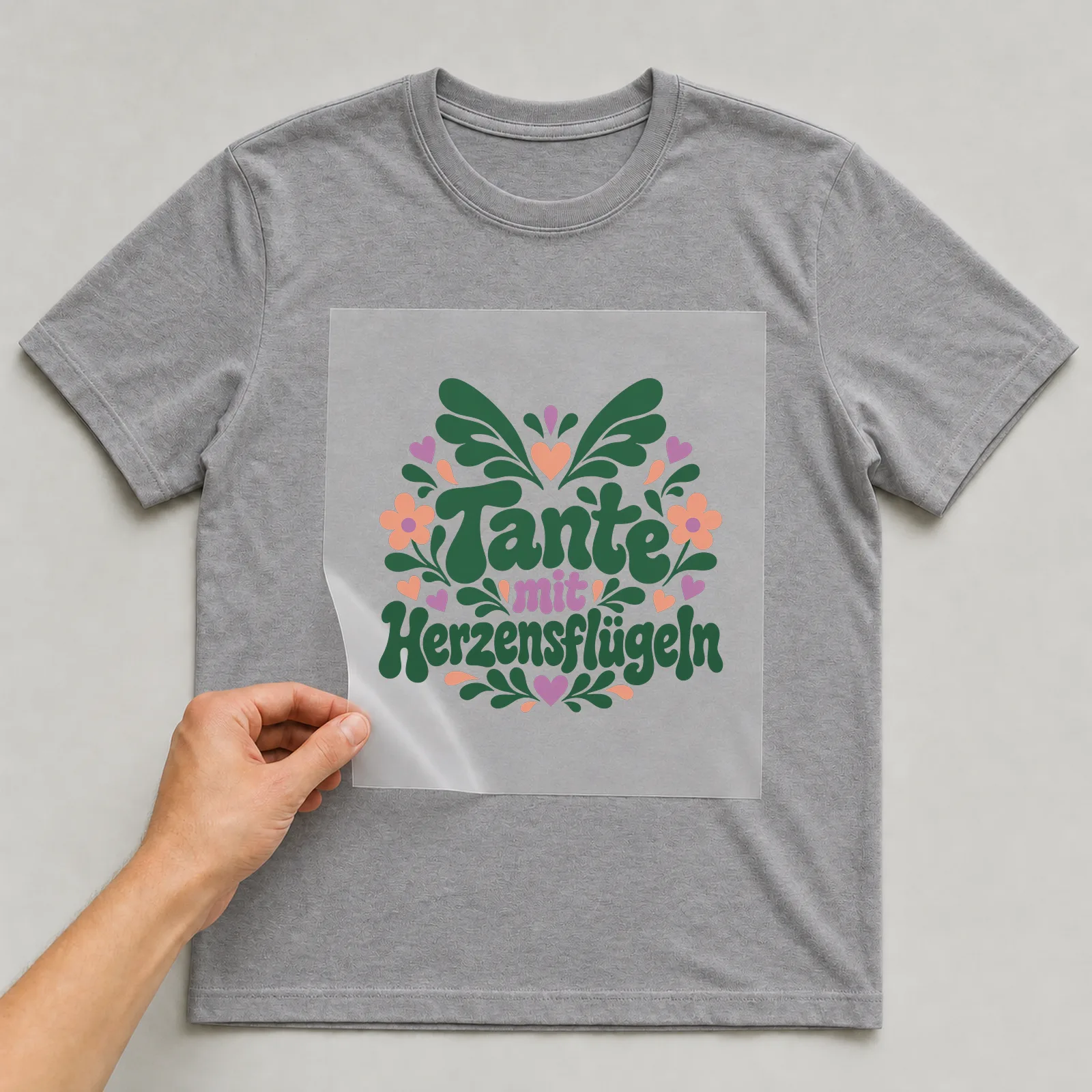 Bügelbild „Tante mit Herzensflügeln“ auf grauem T-Shirt, Folie wird aufgelegt