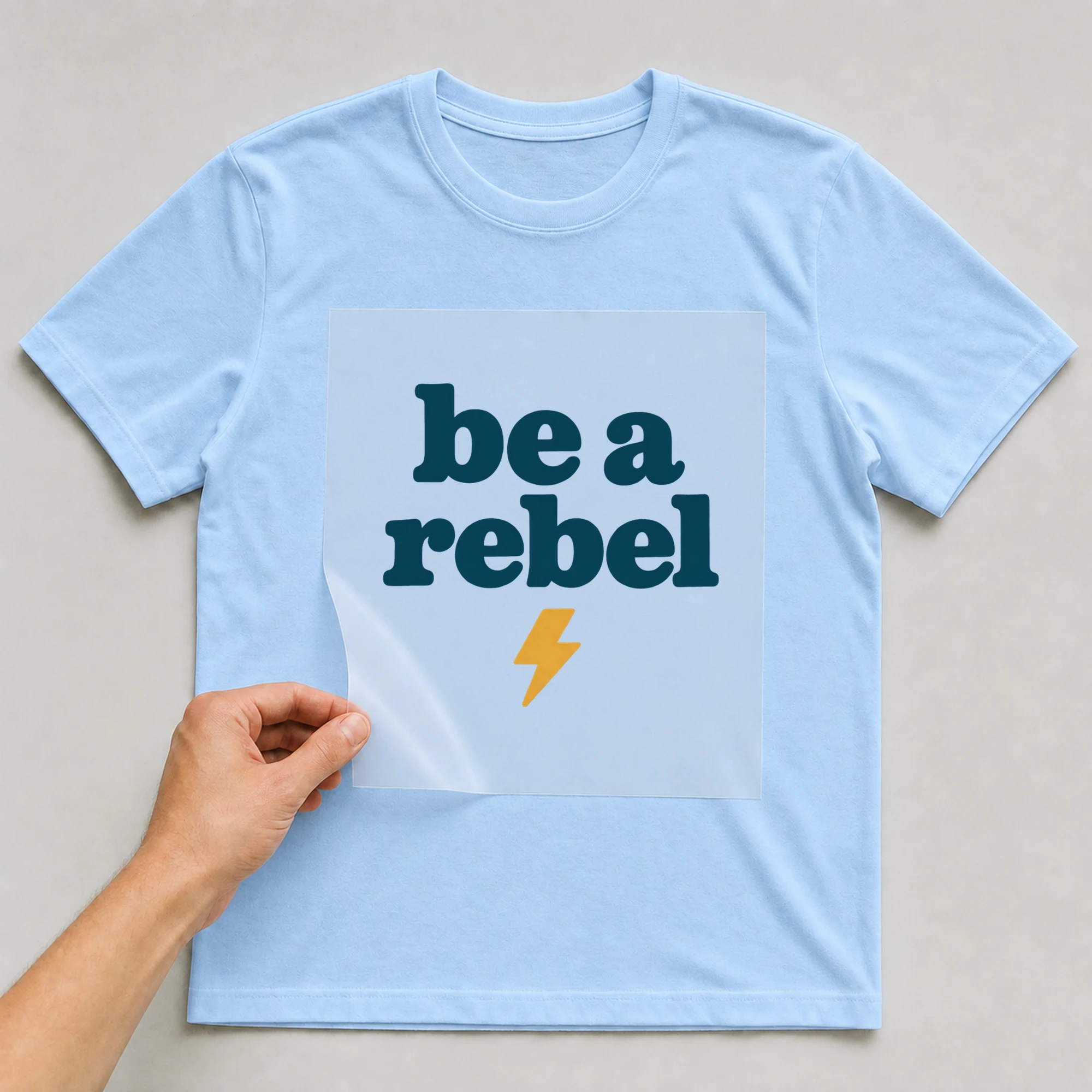 Bügelbild „be a rebel“ auf babyblauem T-Shirt, Folie wird aufgelegt