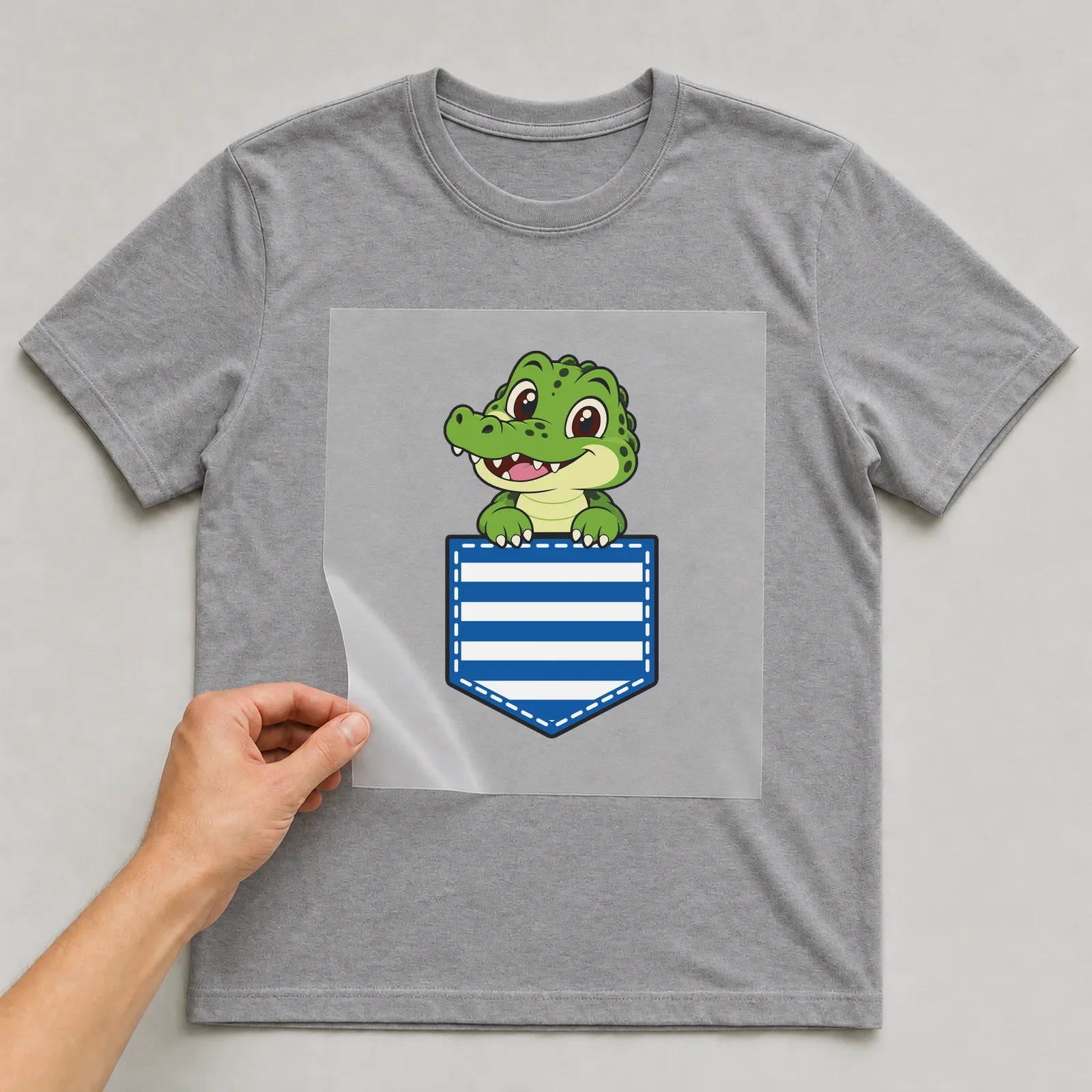 Bügelbild Brusttasche Krokodil auf grauem T-Shirt, Folie wird aufgelegt