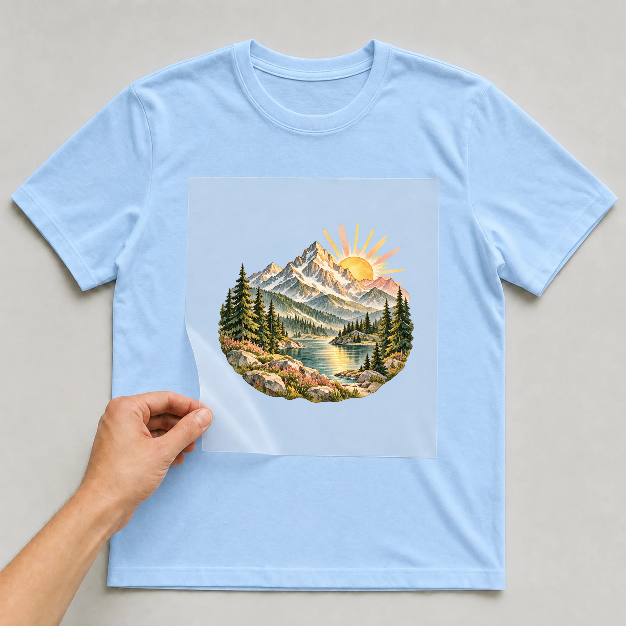 Bügelbild „Berge zum Wandern“ auf babyblauem T-Shirt, Folie wird aufgelegt
