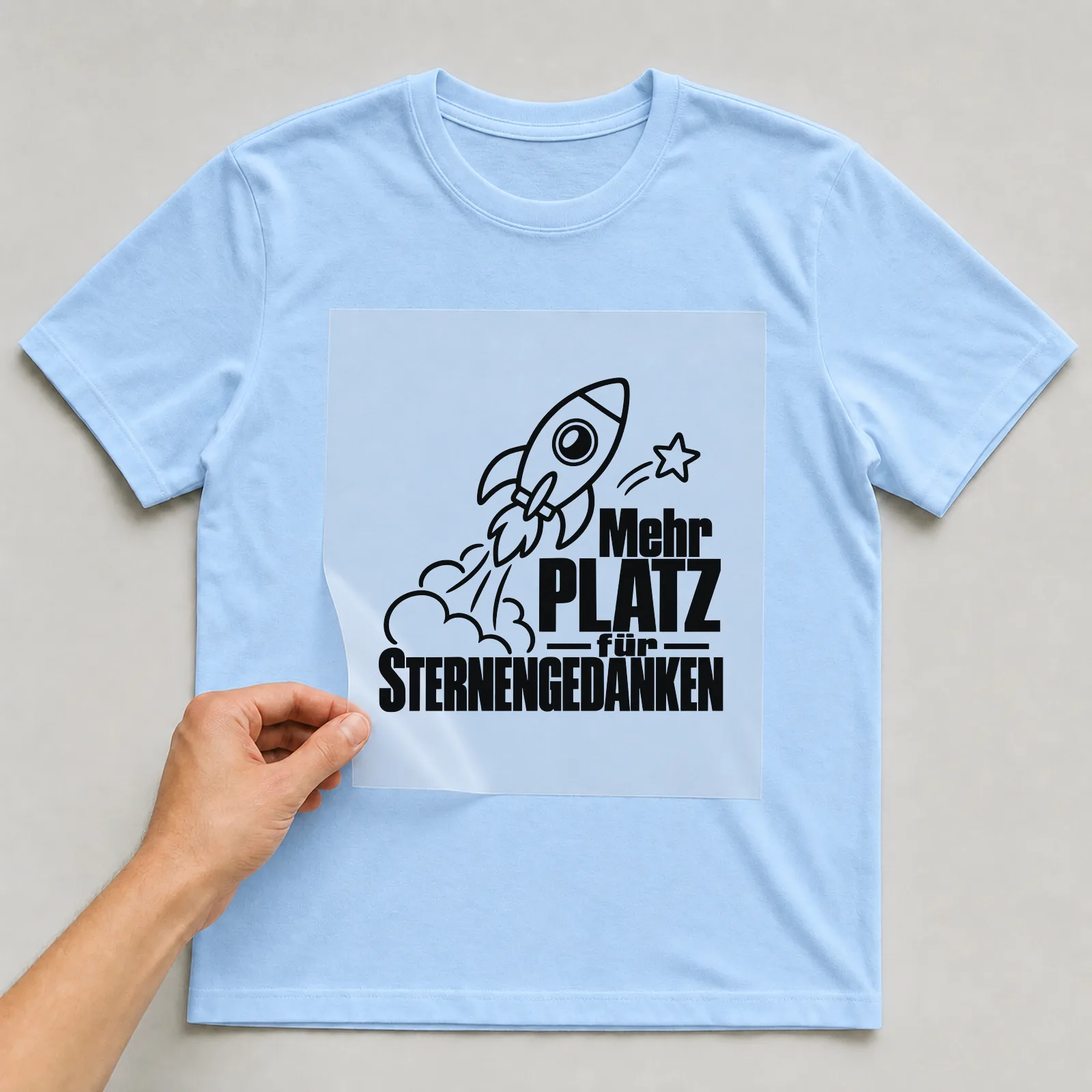 Bügelbild „Mehr Platz für Sternengedanken“ auf hellblauem T-Shirt, Folie wird aufgelegt