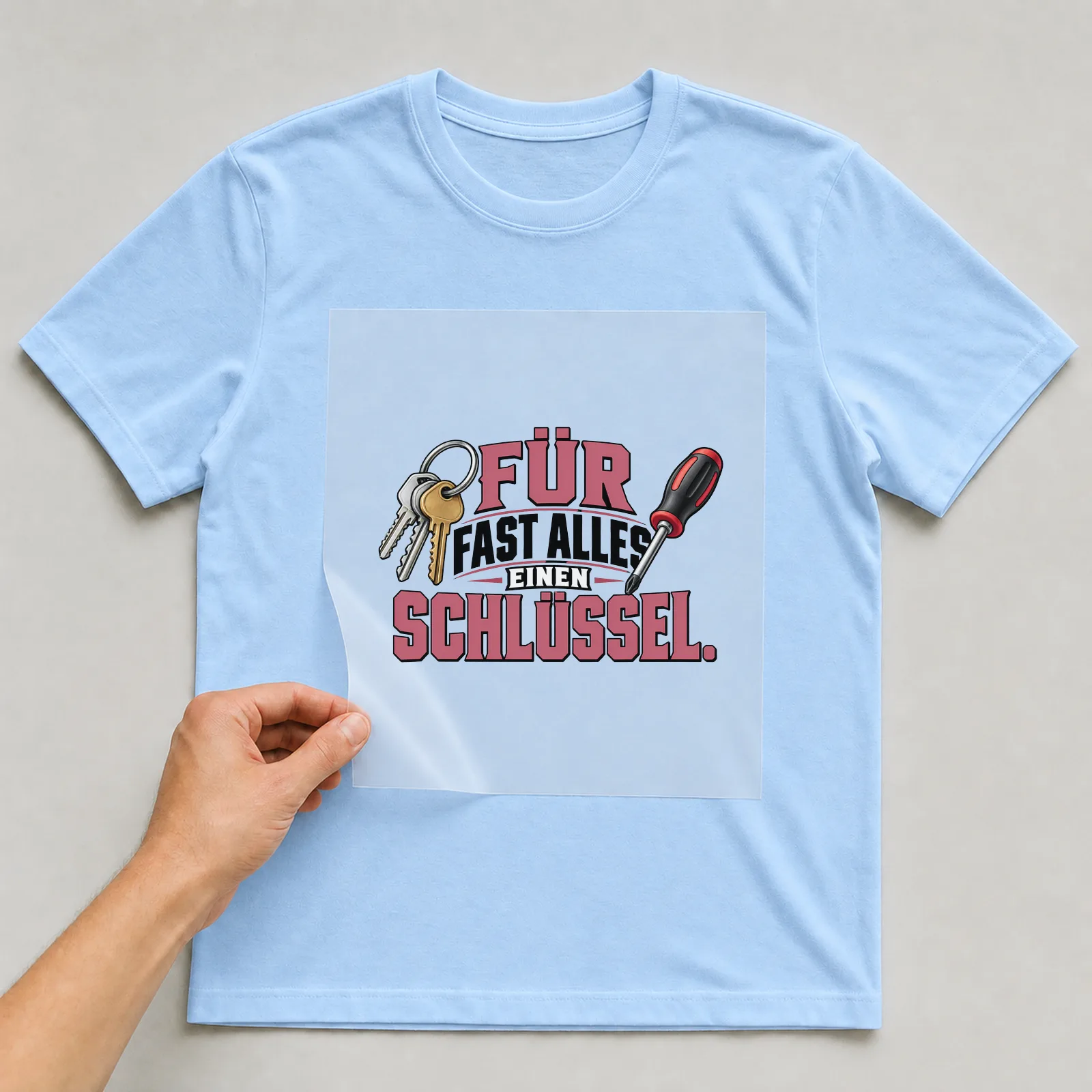 Bügelbild „Für fast alles einen Schlüssel“ auf hellblauem T-Shirt, Folie wird aufgelegt