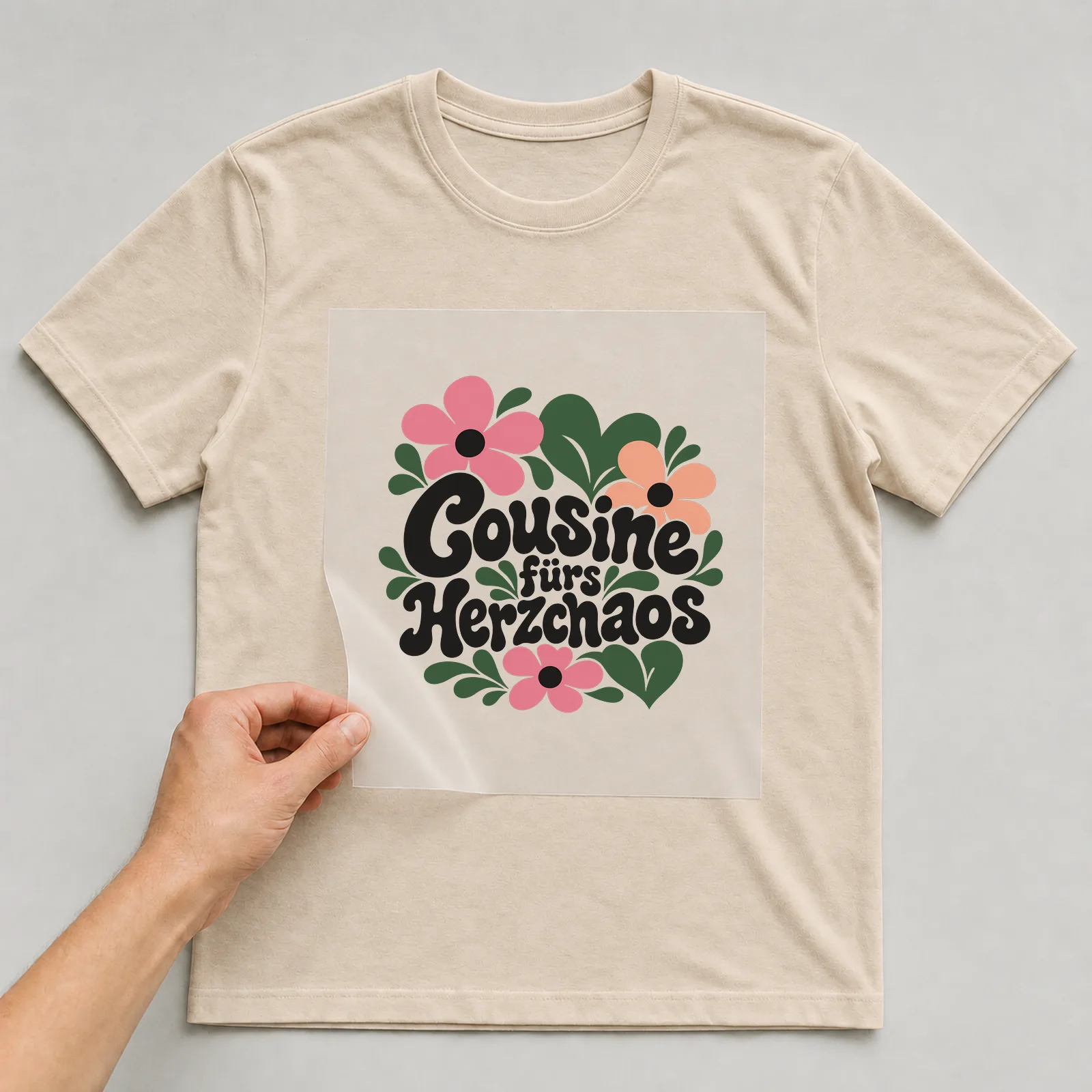 Bügelbild „Cousine fürs Herzchaos“ auf beigem T-Shirt, Folie wird aufgelegt