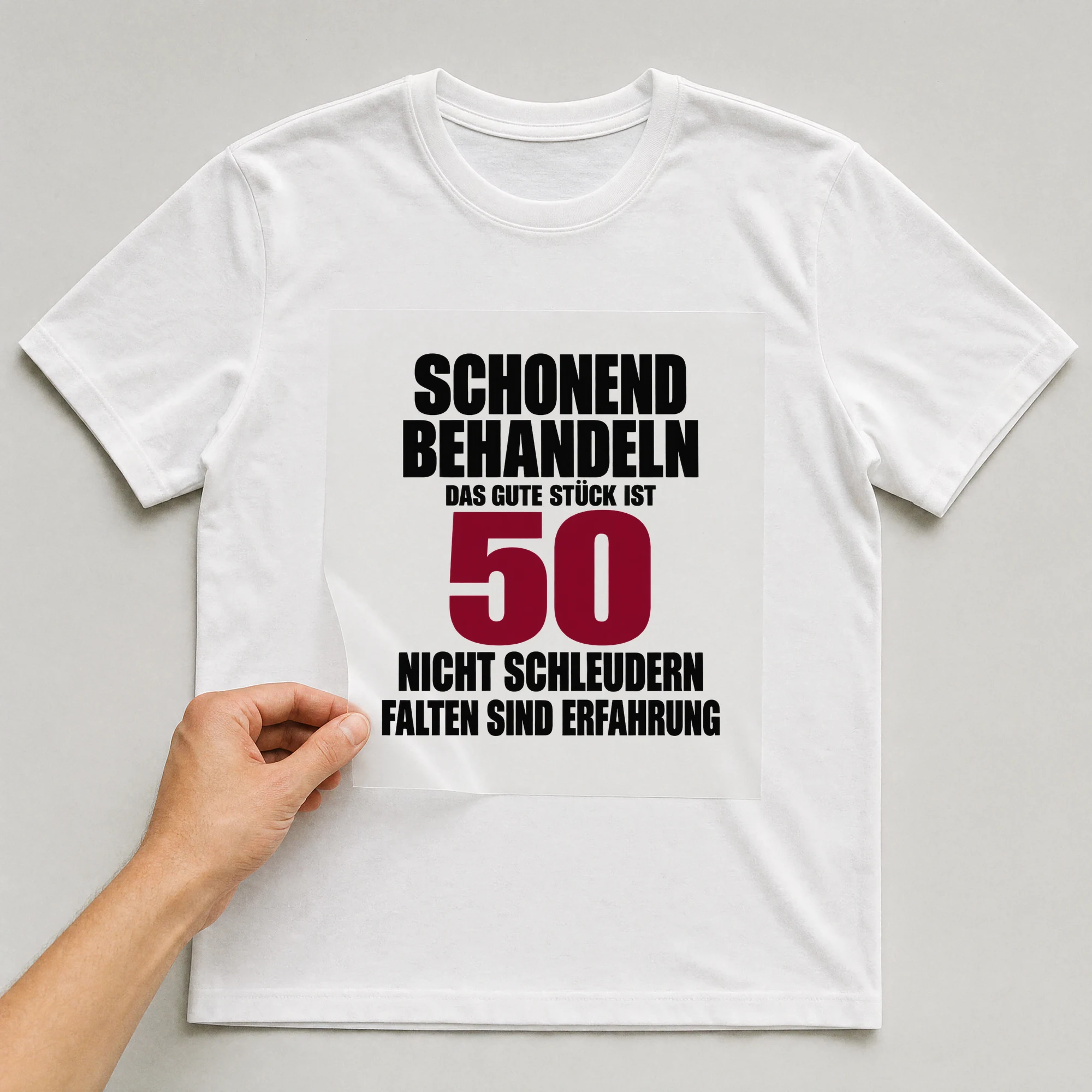 Bügelbild „Schonend behandeln: Das gute Stück ist 50.“ auf weißem T-Shirt, Folie wird aufgelegt