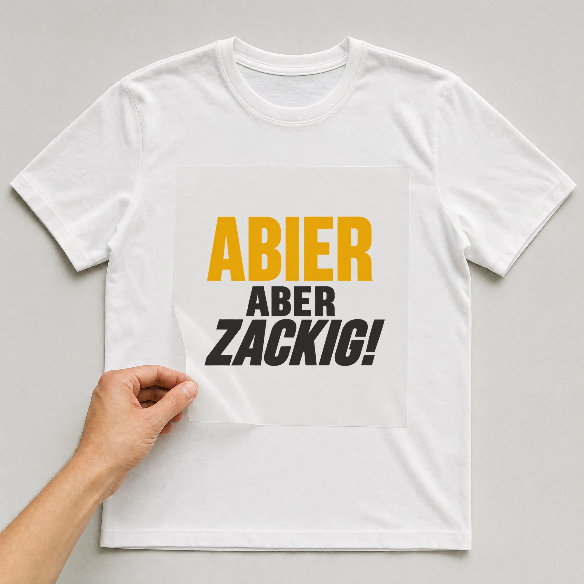 Bügelbild „Abier Aber Zackig!“ auf weißem T-Shirt, Folie wird aufgelegt