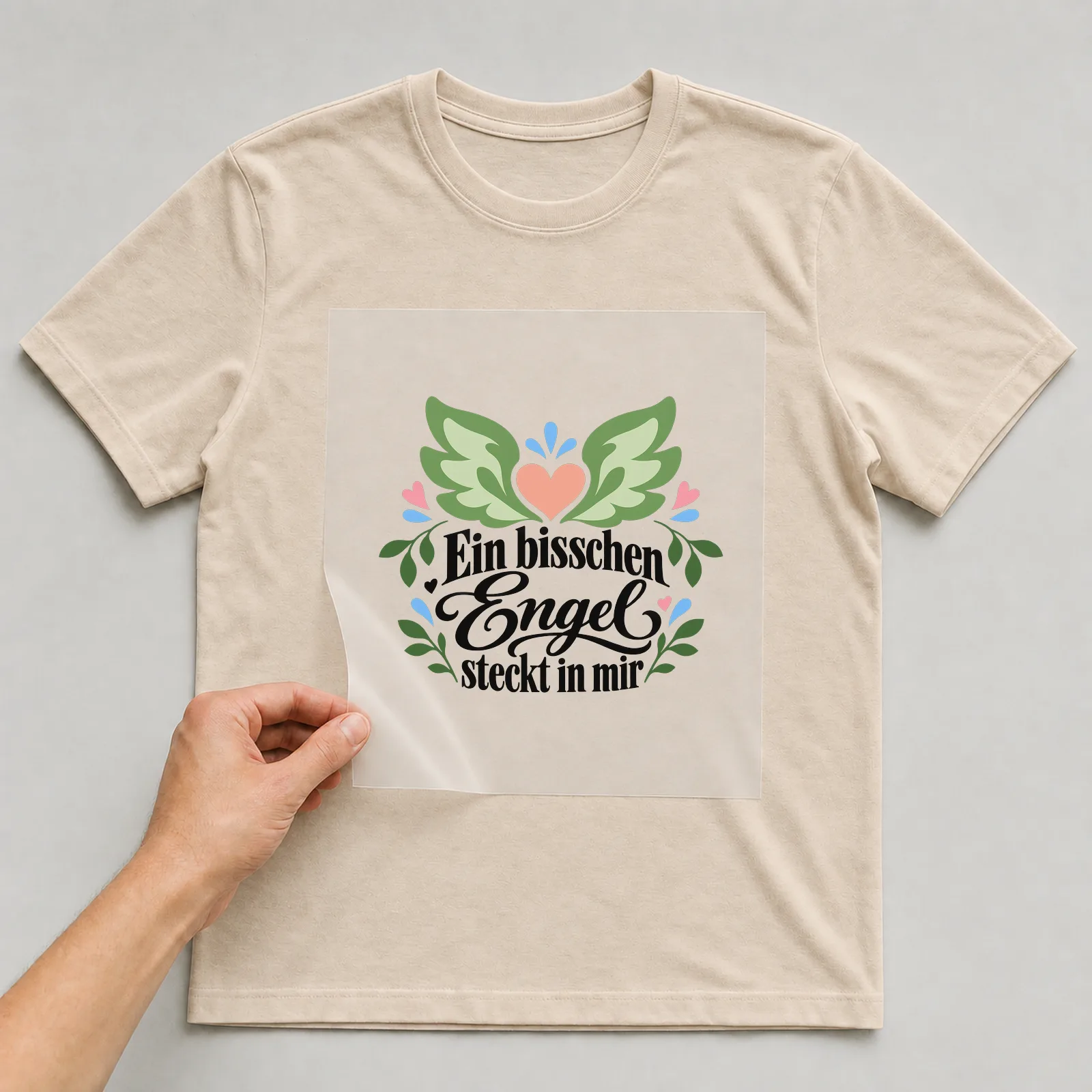 Bügelbild „Ein bisschen Engel steckt in mir“ auf beigem T-Shirt, Folie wird aufgelegt