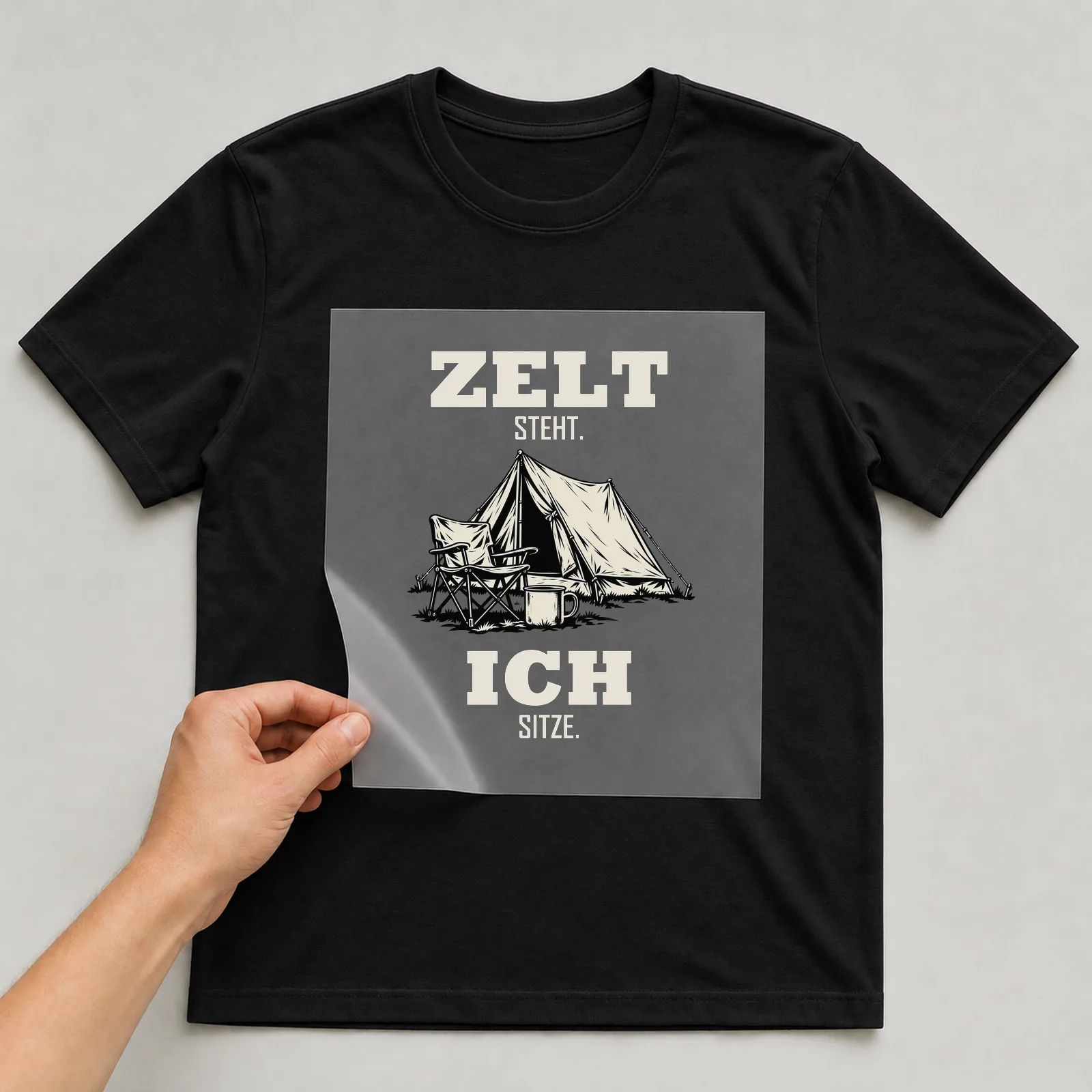 Bügelbild „Zelt steht. Ich sitze.“ auf schwarzem T-Shirt, Folie wird aufgelegt