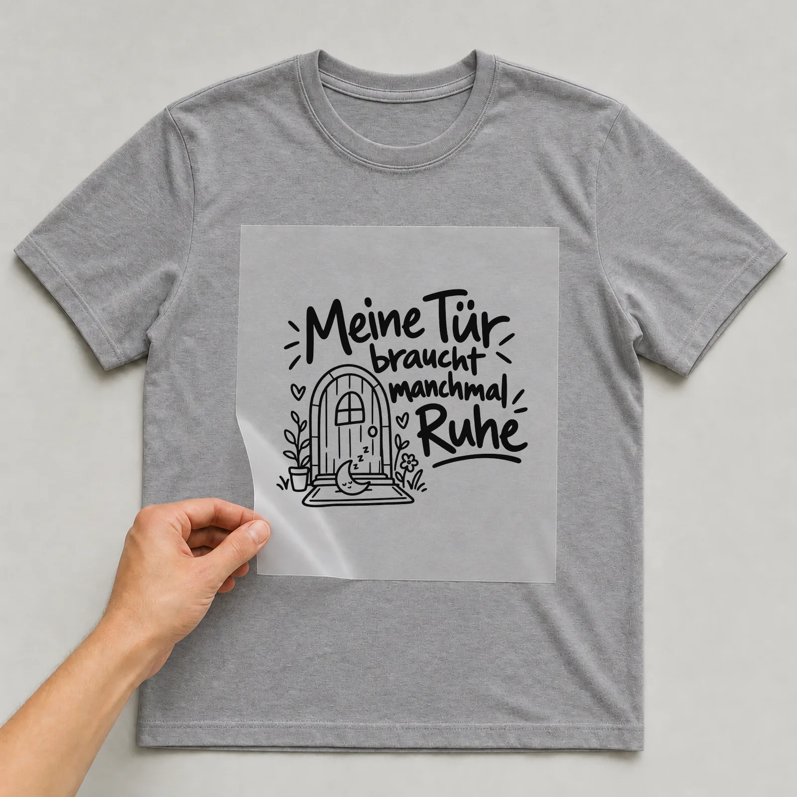 Bügelbild „Meine Tür braucht manchmal Ruhe“ auf grauem T-Shirt, Folie wird aufgelegt