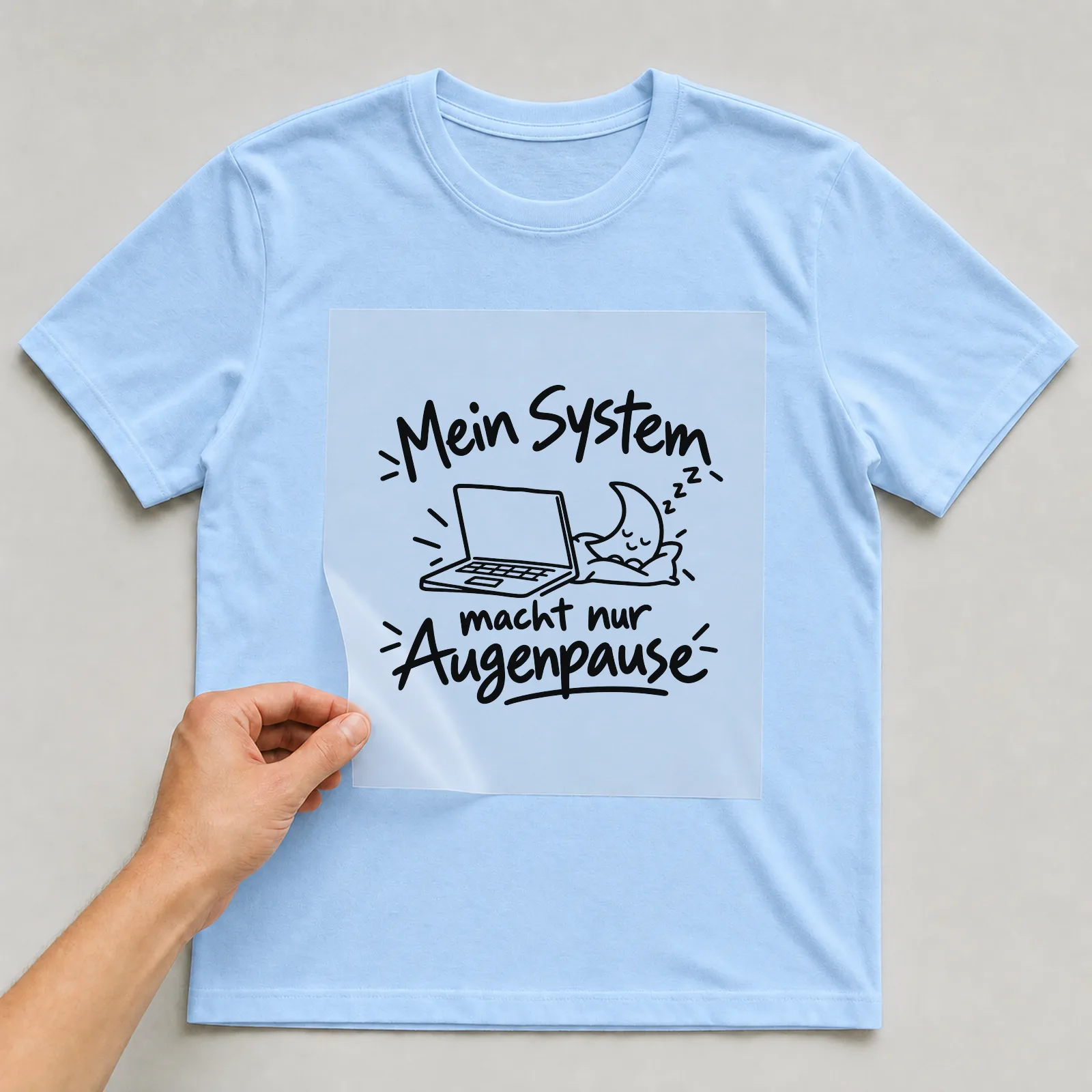 Bügelbild „Mein System macht nur Augenpause“ auf hellblauem T-Shirt, Folie wird aufgelegt