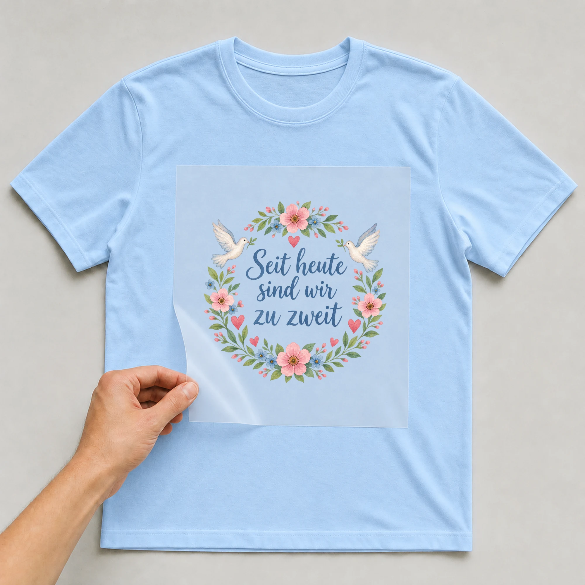 Bügelbild „Seit heute sind wir zu zweit“ auf babyblauem T-Shirt, Folie wird aufgelegt