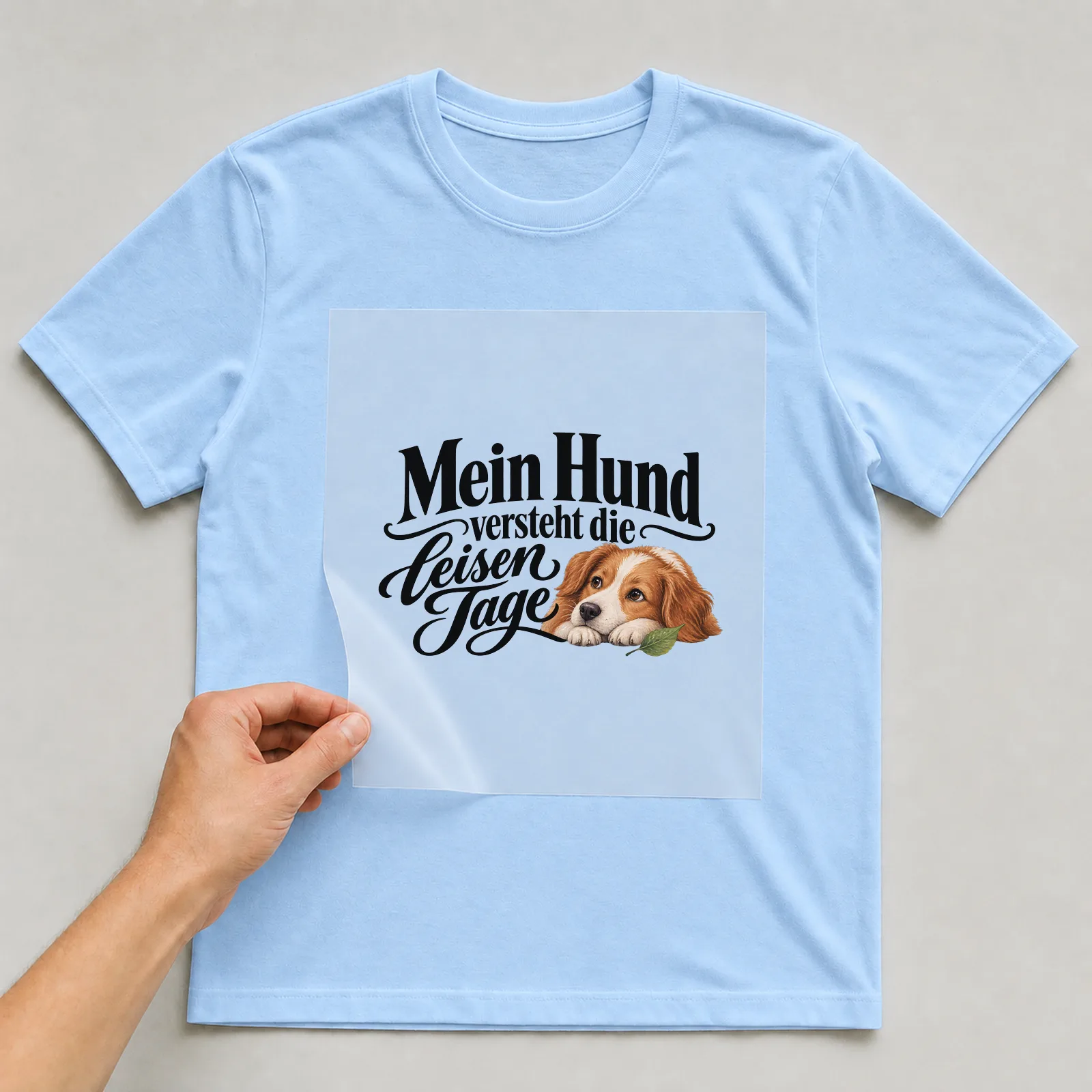 Bügelbild „Mein Hund versteht die leisen Tage“ auf hellblauem T-Shirt, Folie wird aufgelegt