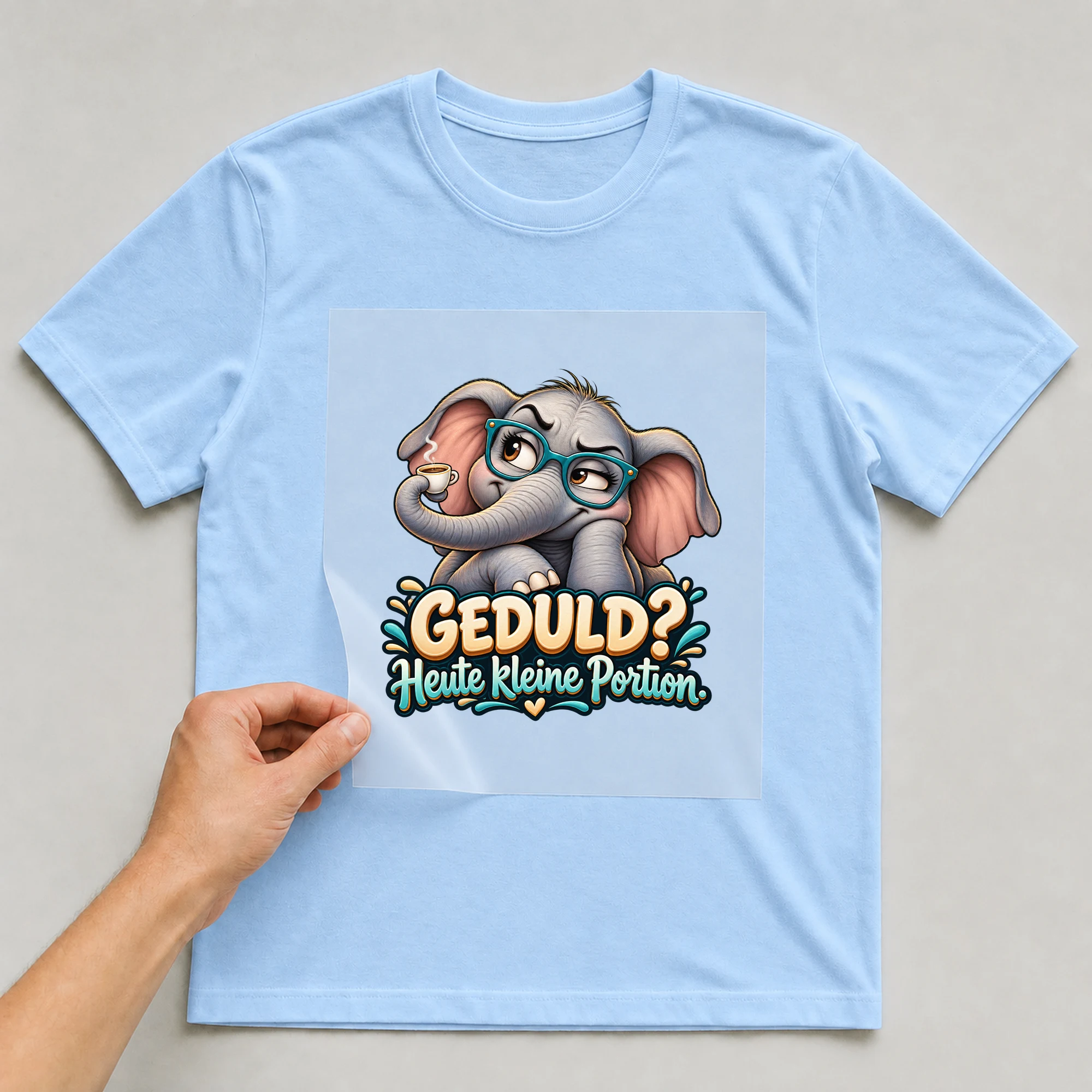 Bügelbild „Geduld? Heute kleine Portion.“ auf babyblauem T-Shirt, Folie wird aufgelegt