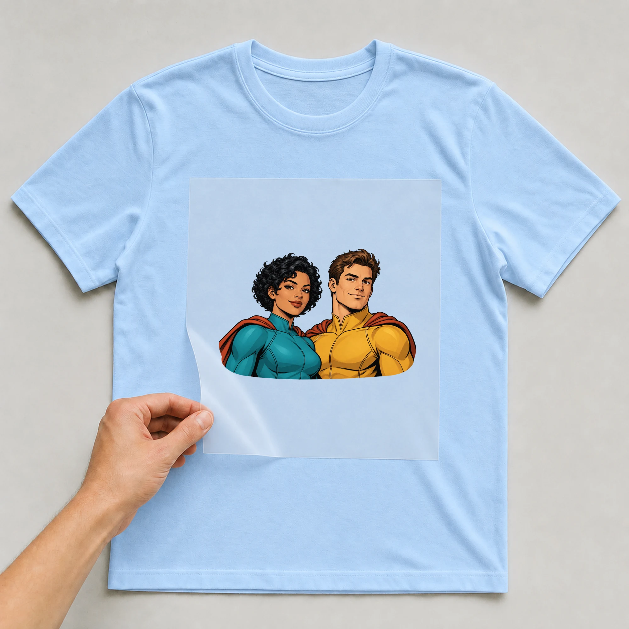 Bügelbild „Superheroes With Cape“ auf babyblauem T-Shirt, Folie wird aufgelegt