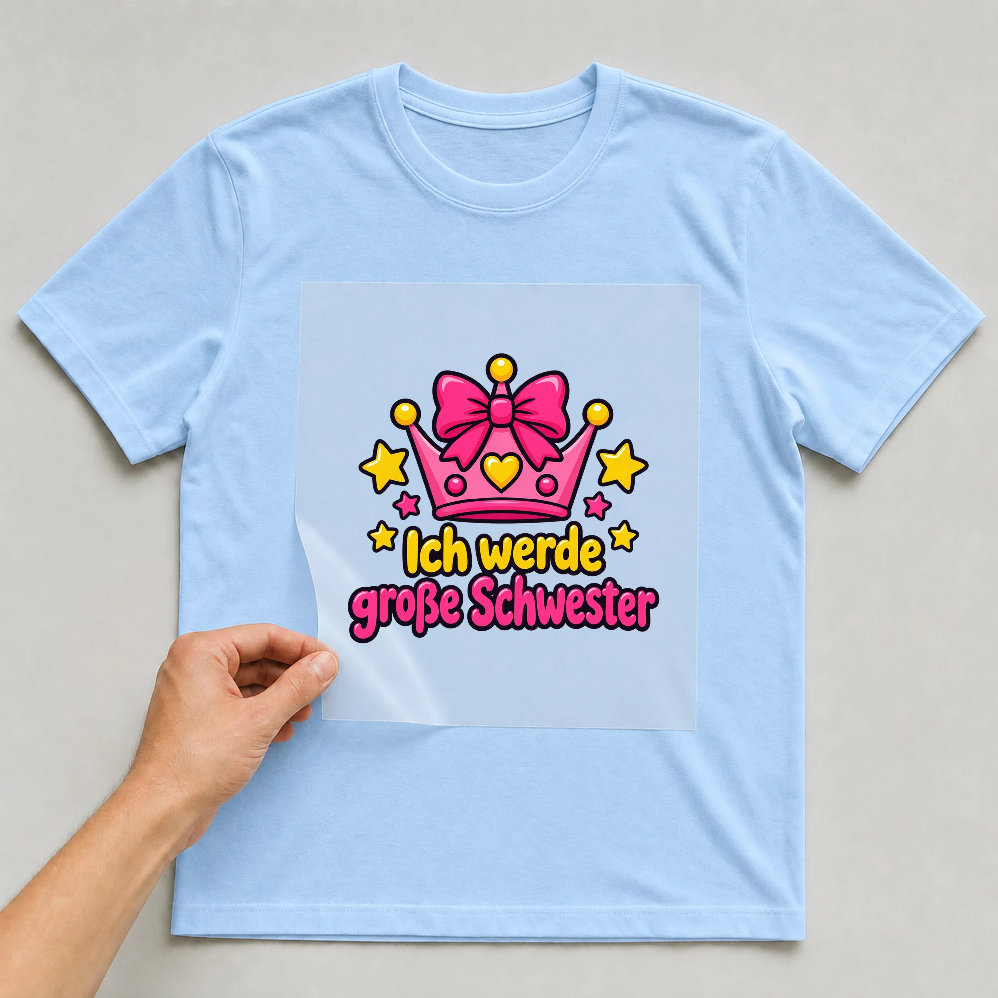 Bügelbild „Ich werde große Schwester“ auf babyblauem T-Shirt, Folie wird aufgelegt