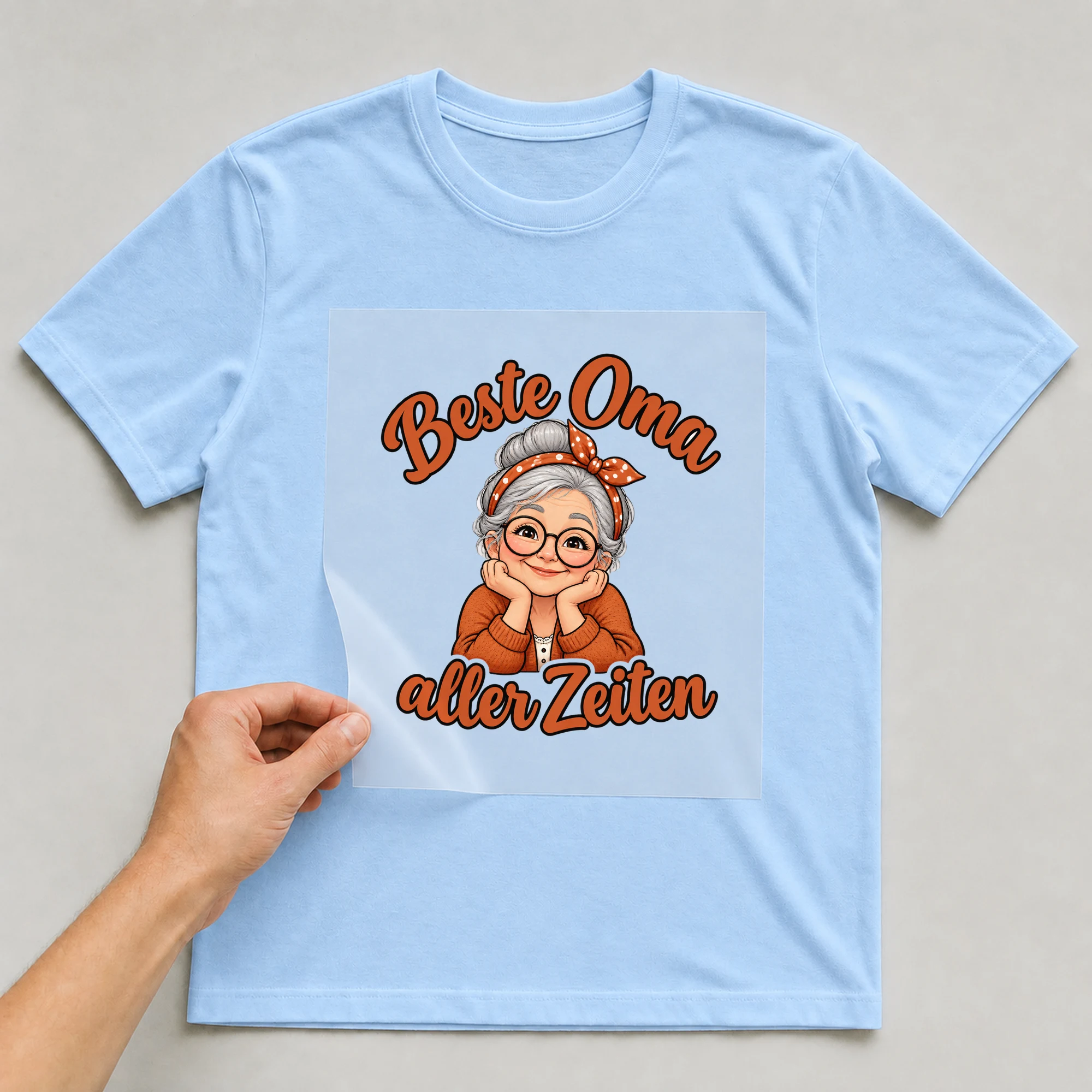 Bügelbild „Beste Oma aller Zeiten“ auf babyblauem T-Shirt, Folie wird aufgelegt