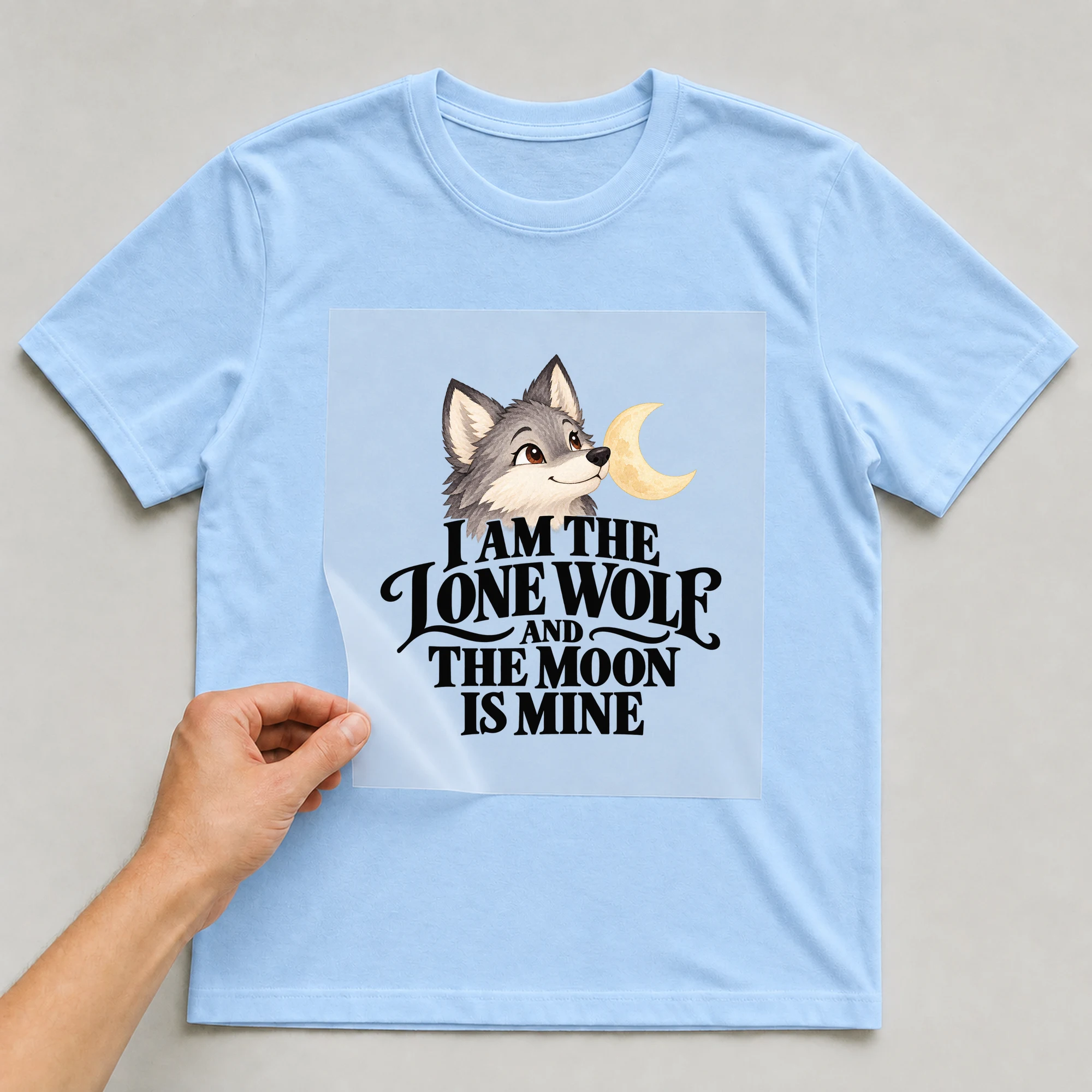 Bügelbild „I Am The Lone Wolf And The Moon Is Mine“ auf babyblauem T-Shirt, Folie wird aufgelegt