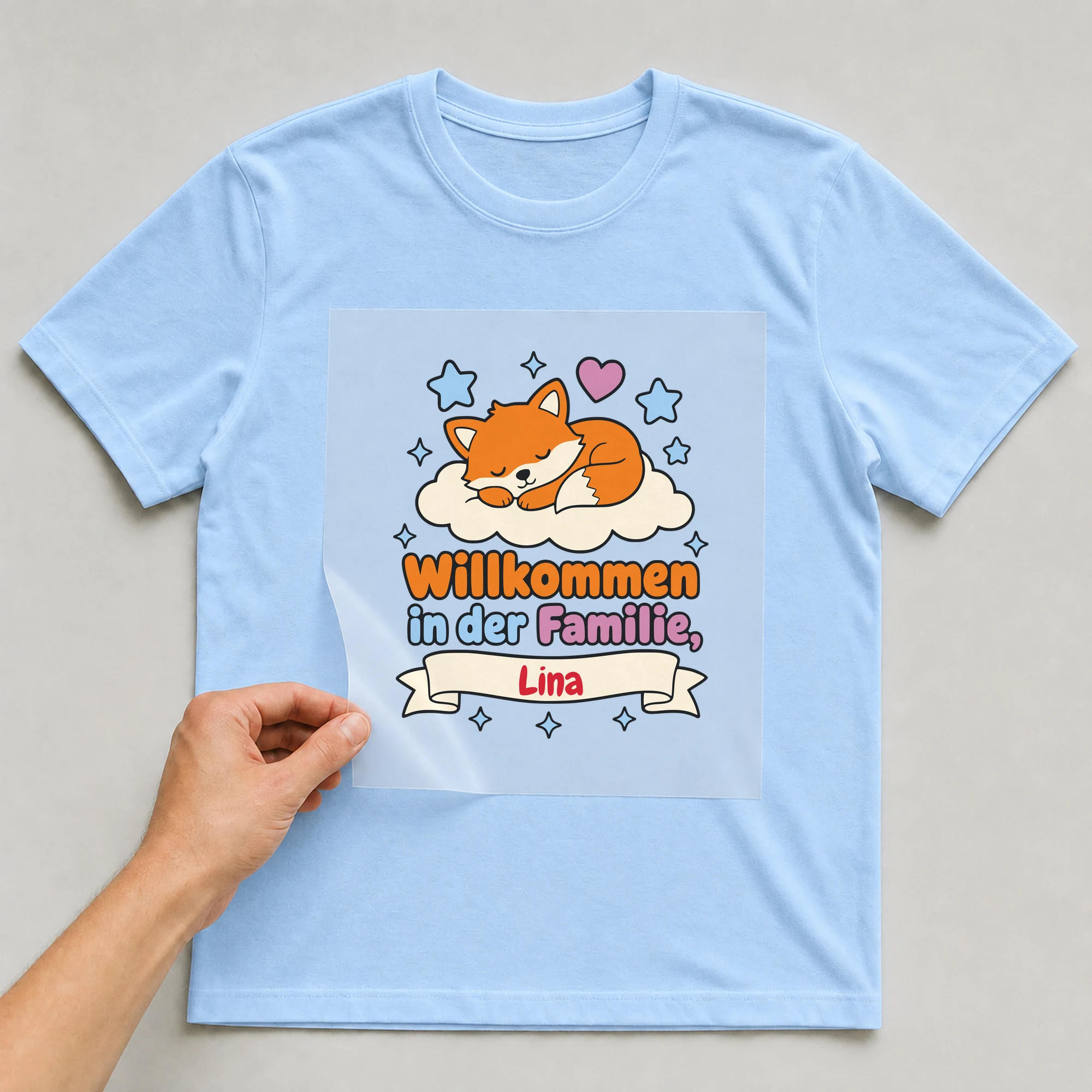 Bügelbild Willkommen in der Familie mit Name auf hellblauem T-Shirt, Folie wird aufgelegt