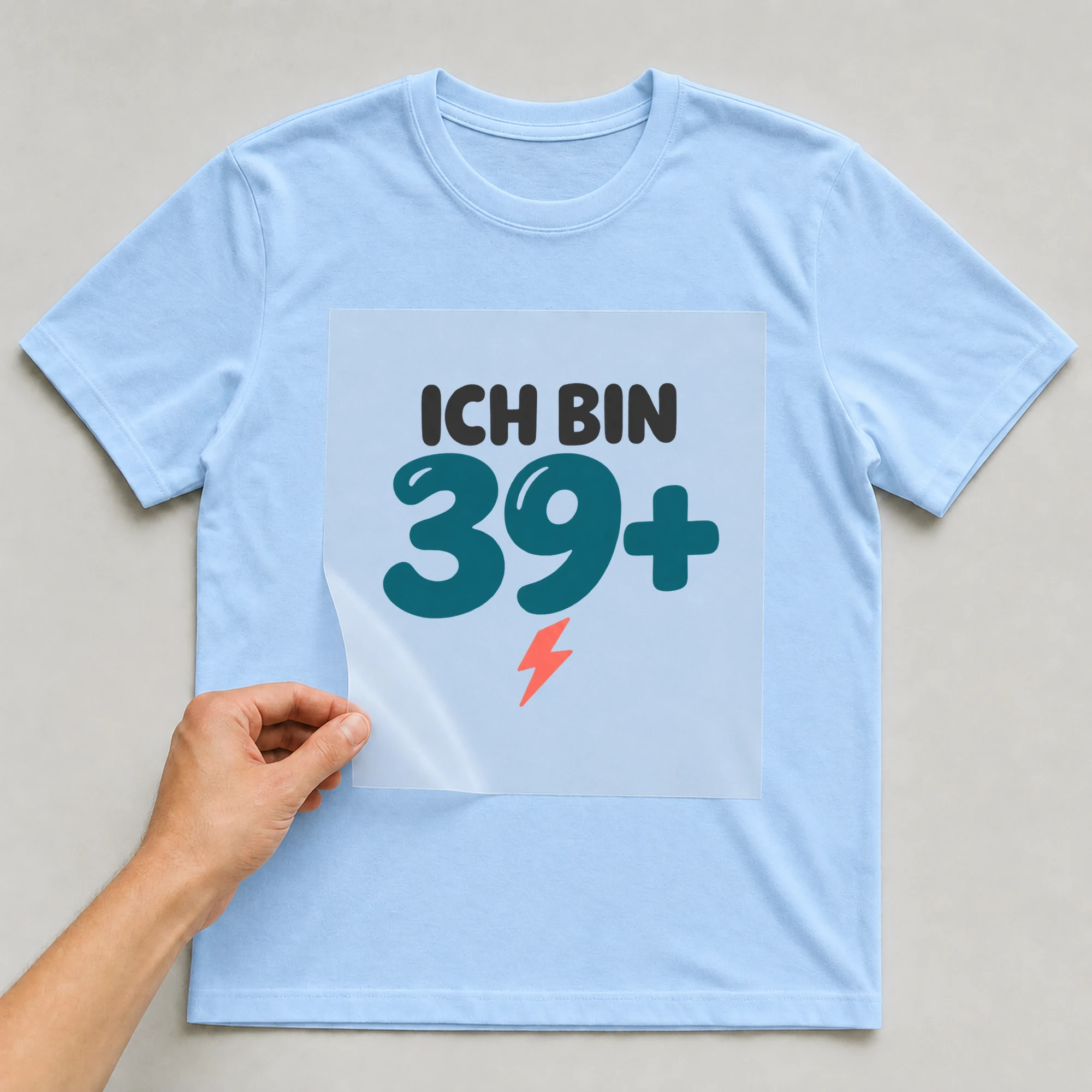 Bügelbild „Ich bin 39+“ auf babyblauem T-Shirt, Folie wird aufgelegt