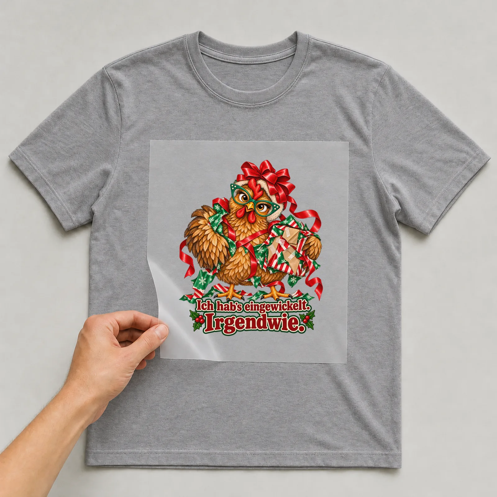 Bügelbild huhn geschenkchaos auf grauem T-Shirt, Folie wird aufgelegt