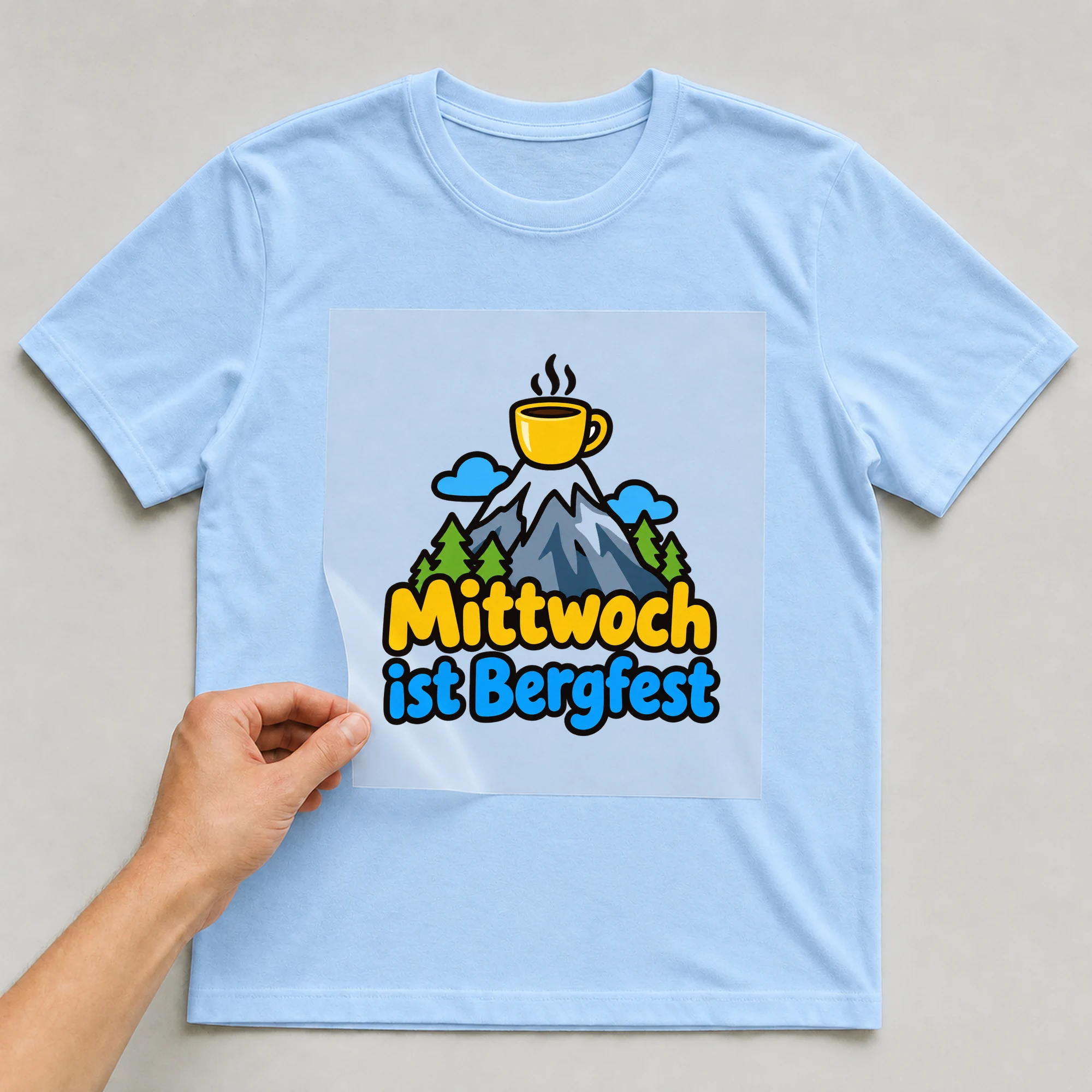 Bügelbild „Mittwoch ist Bergfest“ auf babyblauem T-Shirt, Folie wird aufgelegt