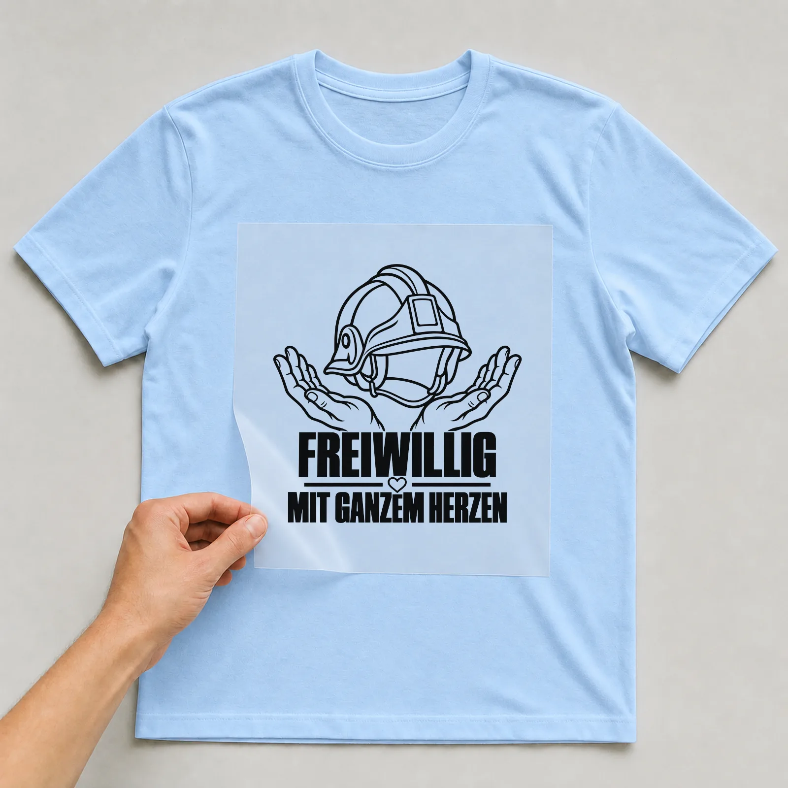 Bügelbild „Freiwillig mit Ganzem herzen“ auf hellblauem T-Shirt, Folie wird aufgelegt