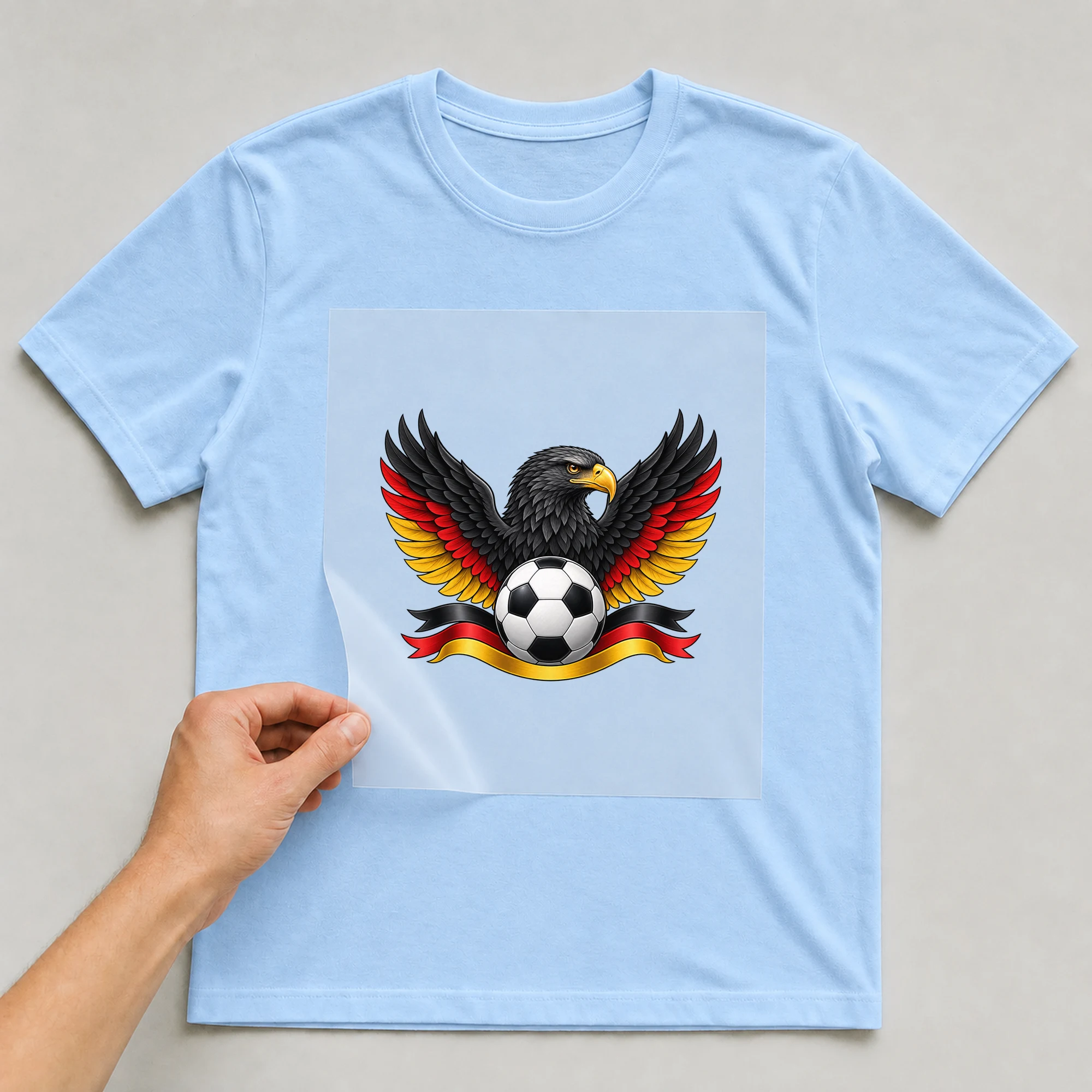 Bügelbild „Fußball Deutschland Adler“ auf babyblauem T-Shirt, Folie wird aufgelegt