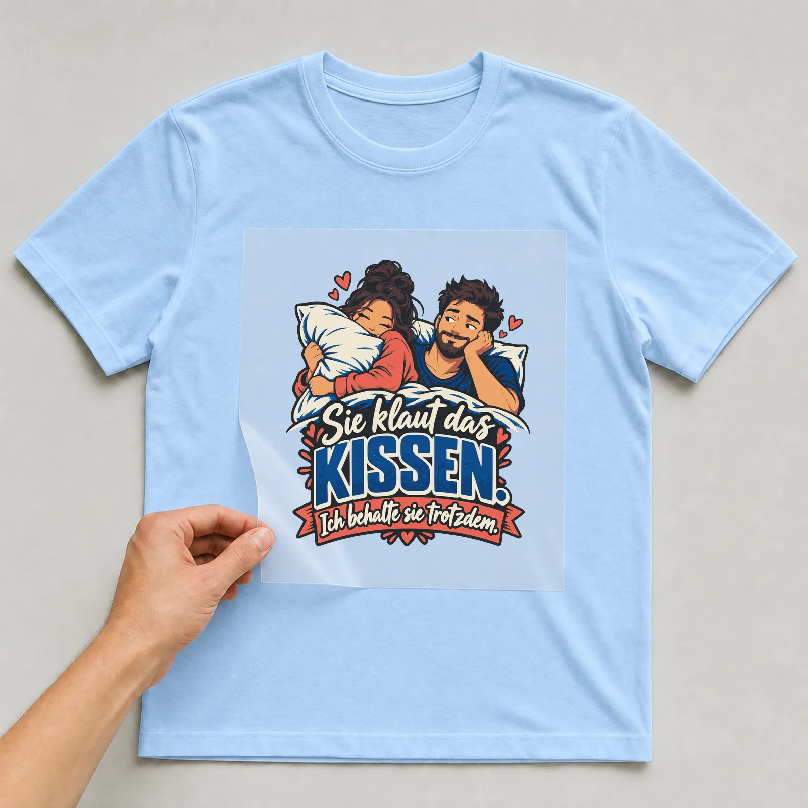 Bügelbild Sie klaut das Kissen. Ich behalte sie trotzdem. (Partnermotiv) auf hellblauem T-Shirt, Folie wird aufgelegt