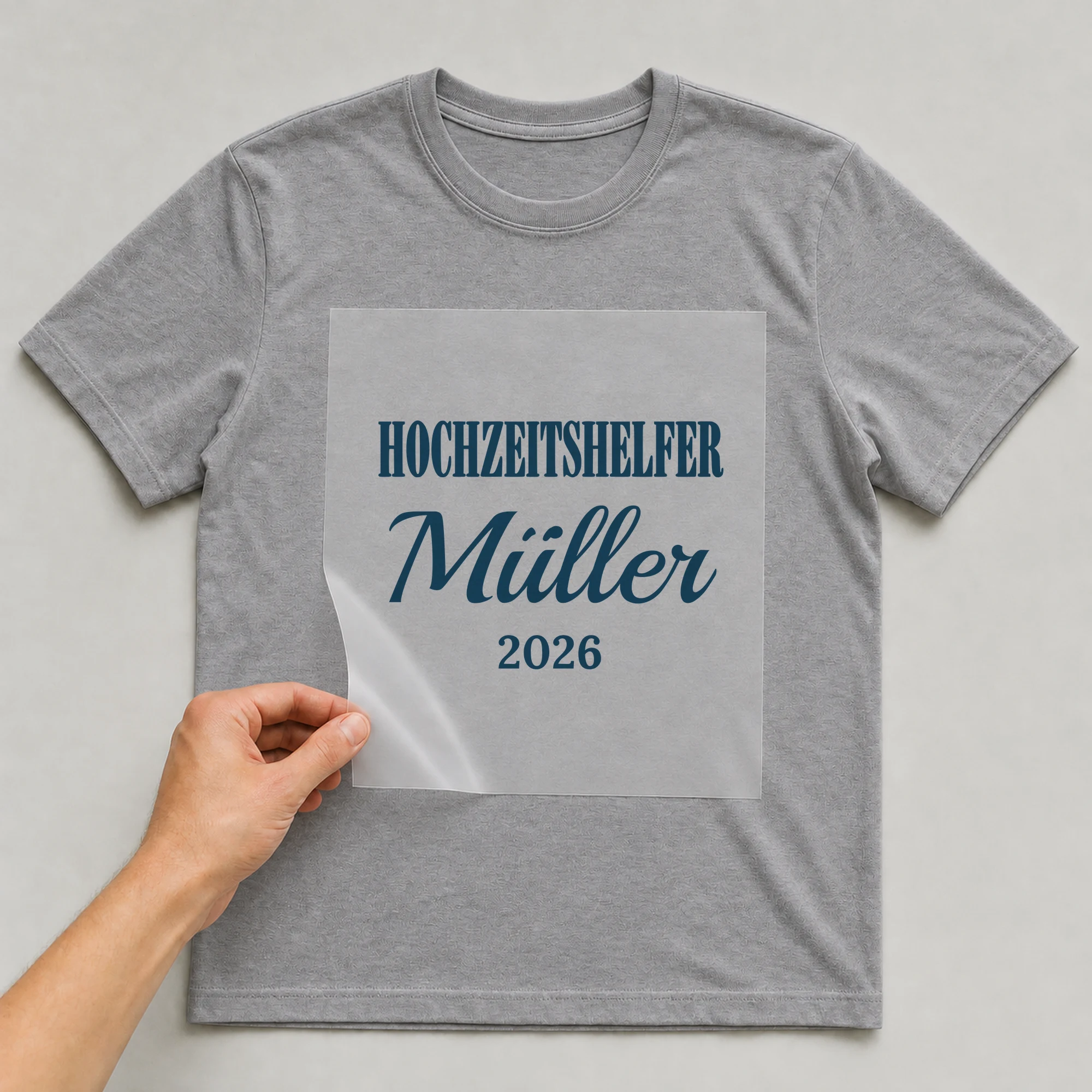 Bügelbild Hochzeitshelfer mit Nachname und Jahr auf grauem T-Shirt, Folie wird aufgelegt