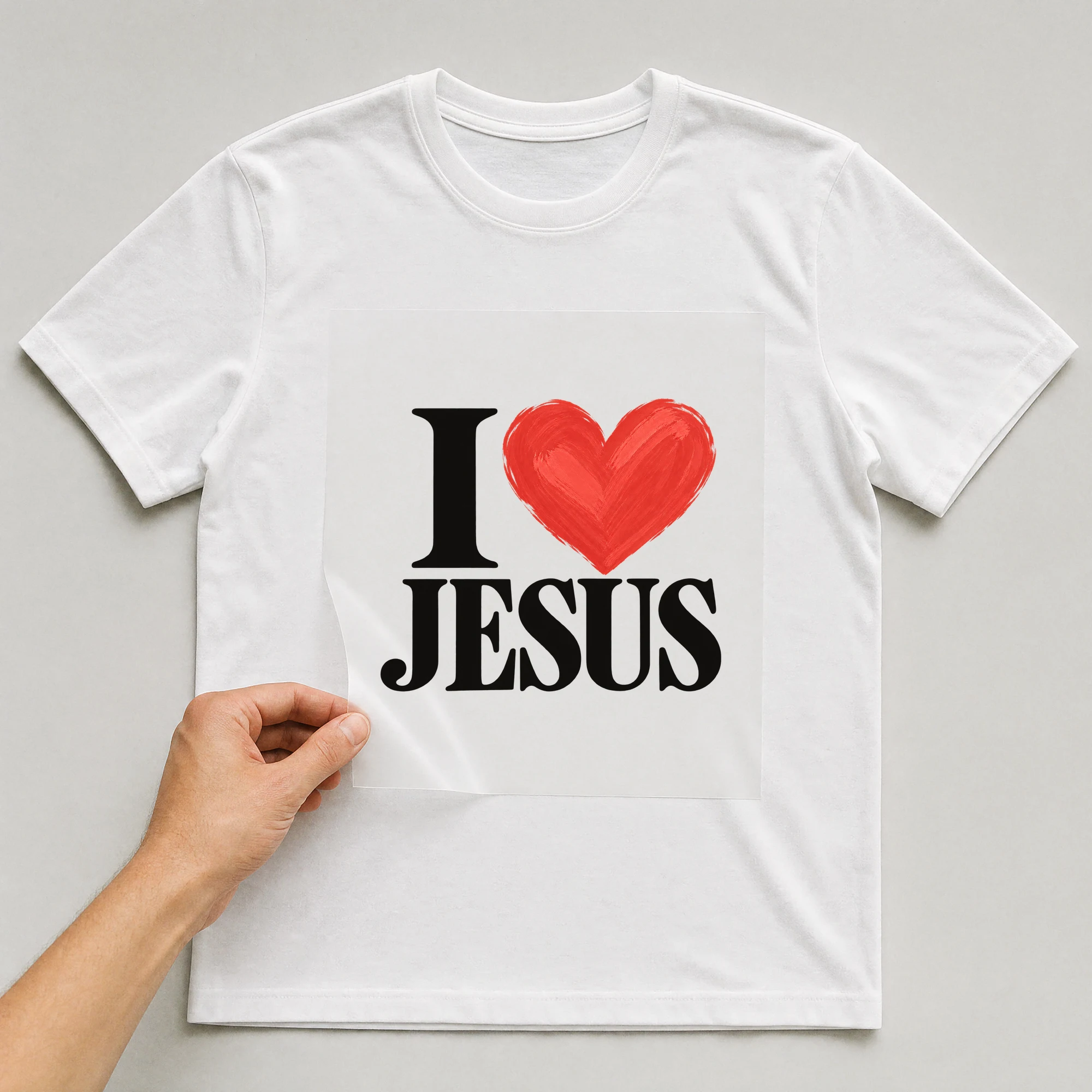Bügelbild „I Herz JESUS“ auf weißem T-Shirt, Folie wird aufgelegt