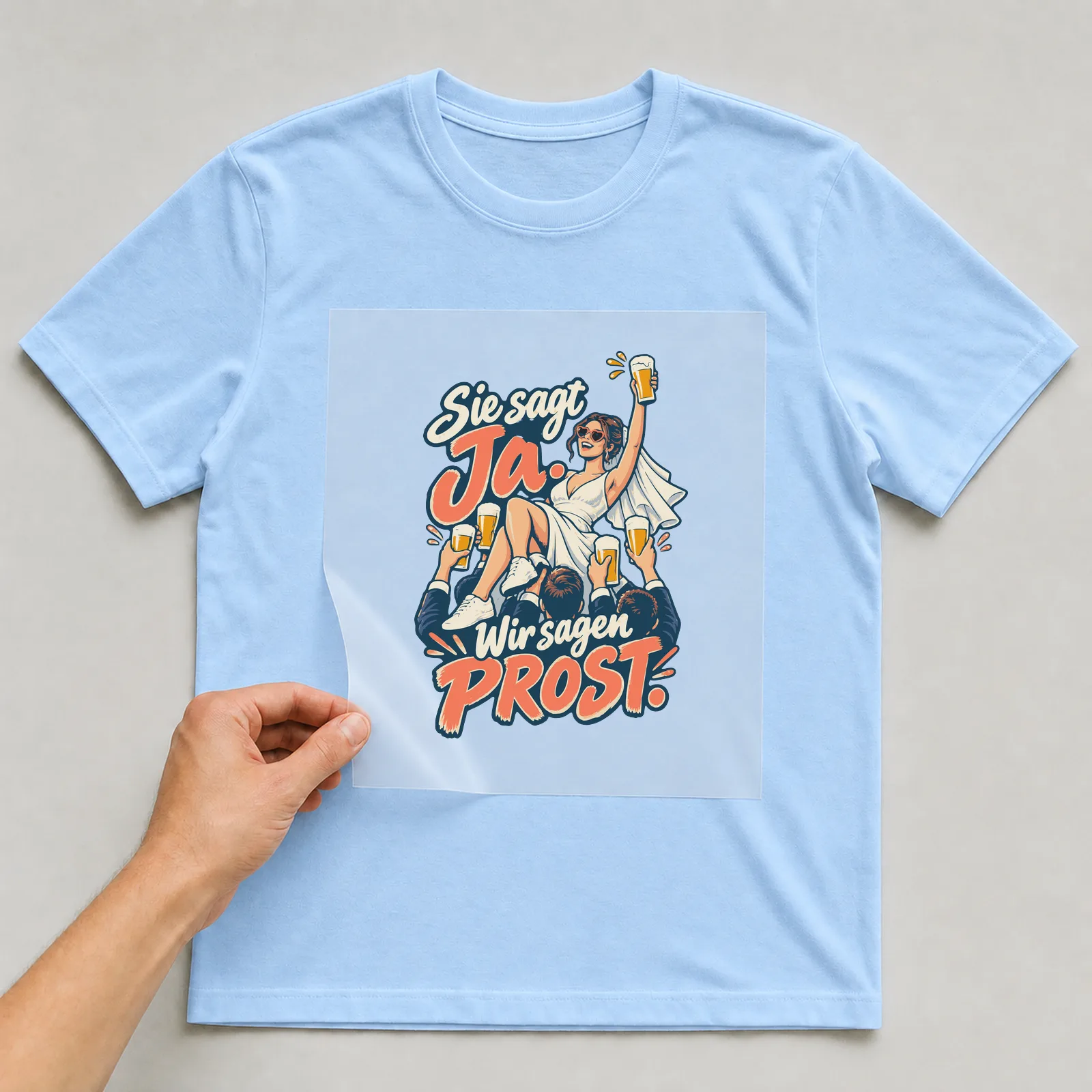 Bügelbild Sie sagt Ja. Wir sagen Prost. auf hellblauem T-Shirt, Folie wird aufgelegt