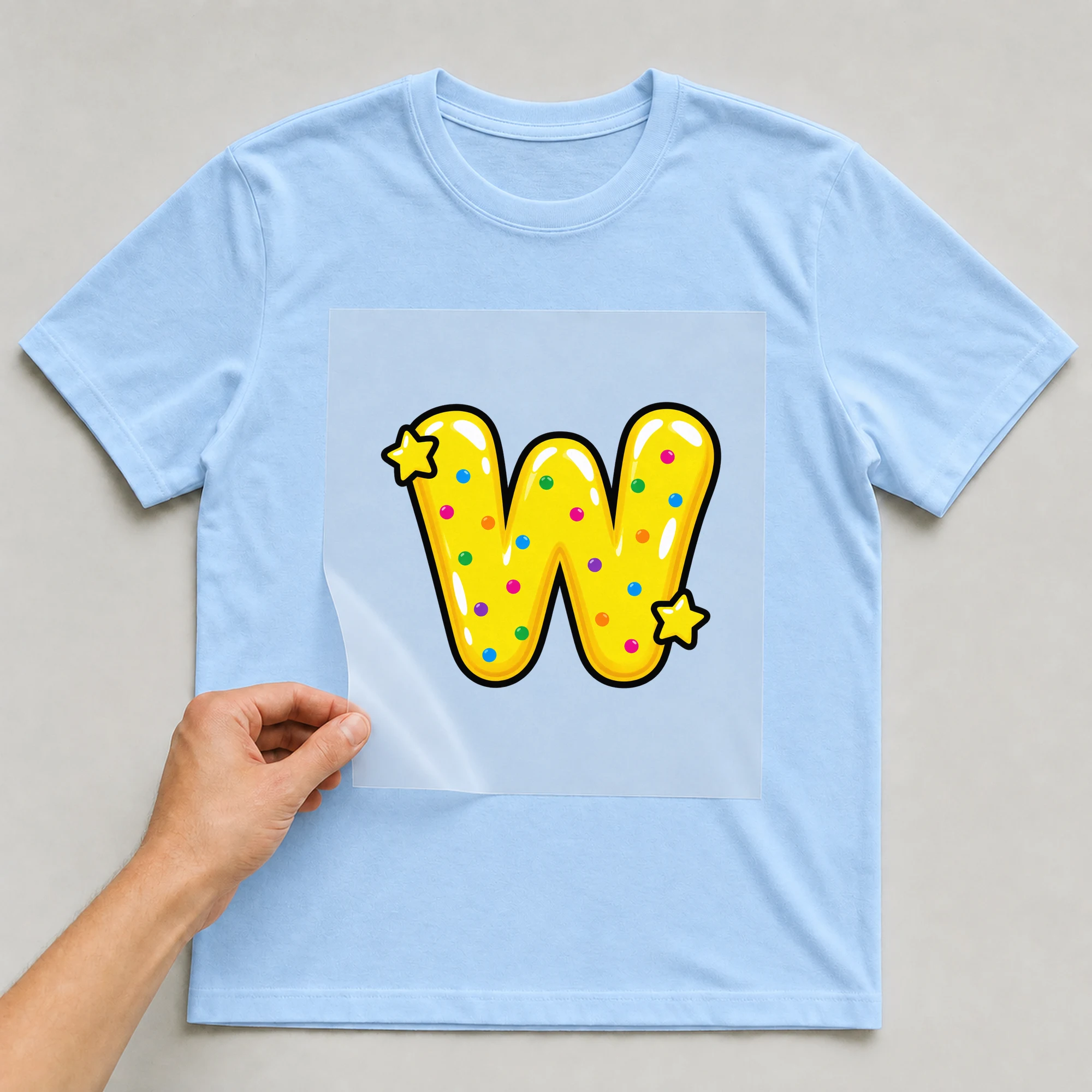 Bügelbild „Buchstabe W im Comic-Ballon-Stil“ auf babyblauem T-Shirt, Folie wird aufgelegt