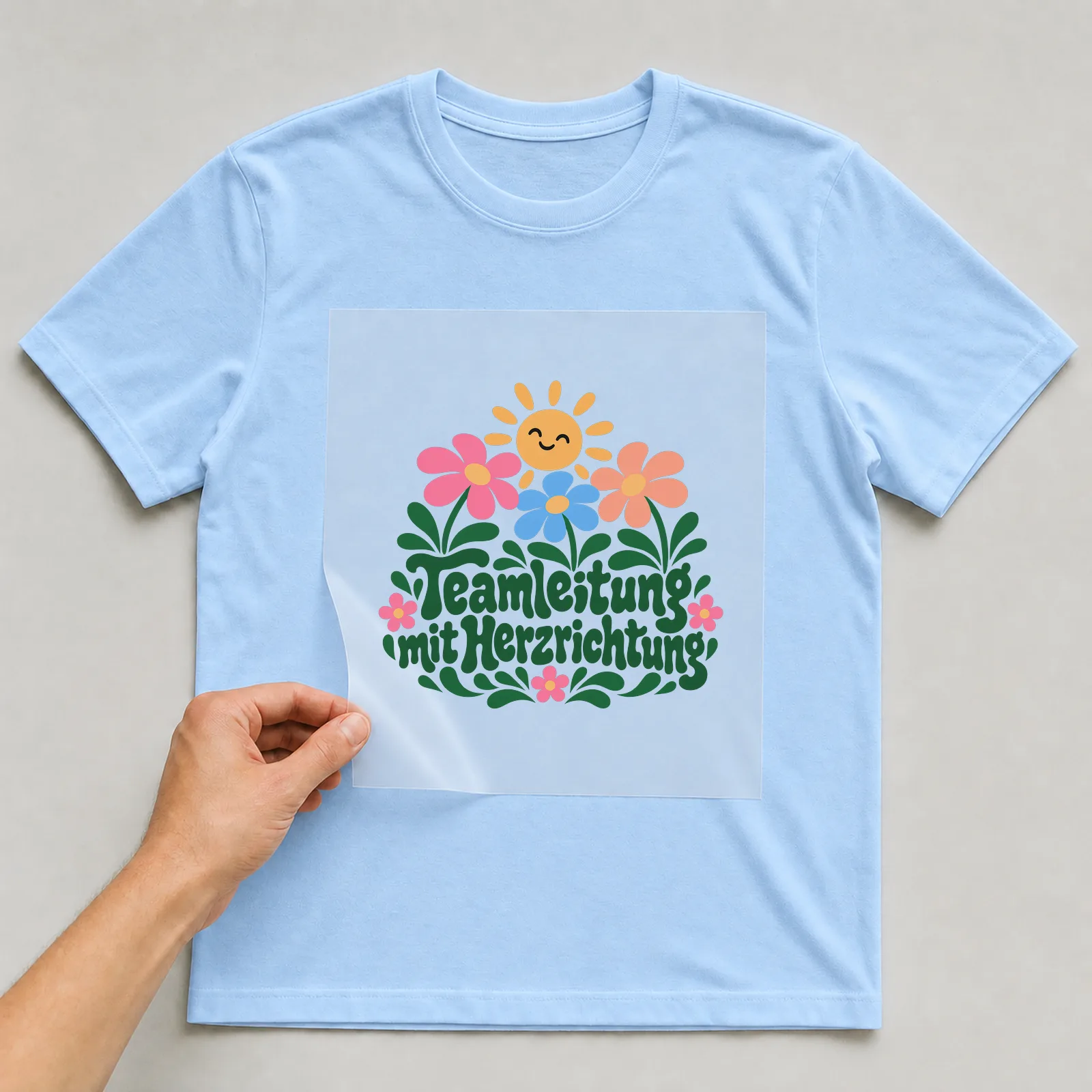 Bügelbild „Teamleitung mit Herzrichtung“ auf hellblauem T-Shirt, Folie wird aufgelegt