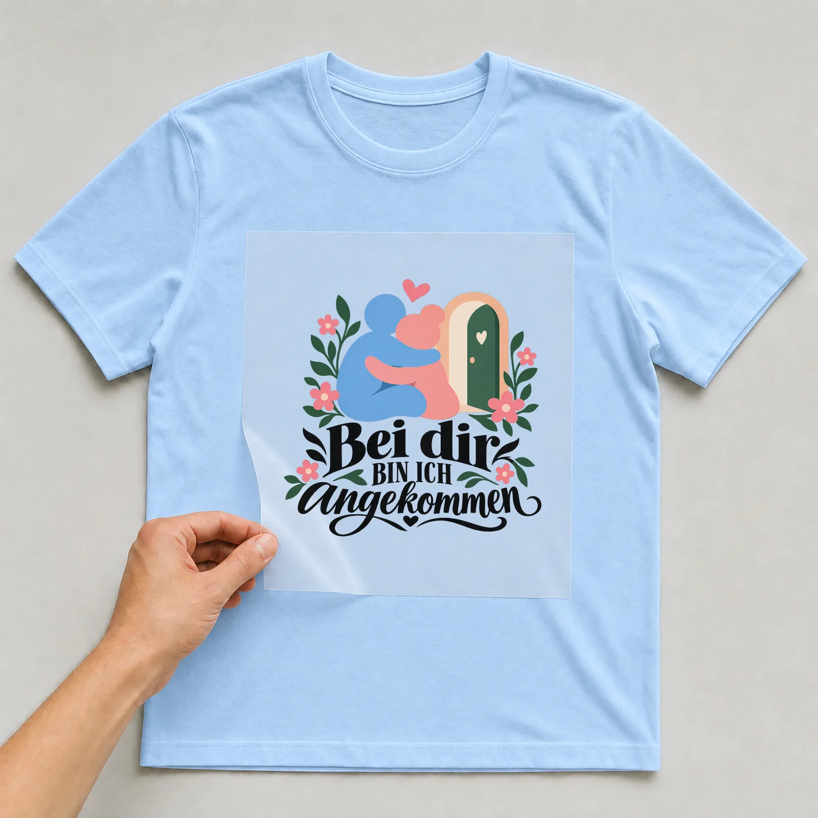 Bügelbild „Bei dir BIN ICH angekommen“ auf hellblauem T-Shirt, Folie wird aufgelegt