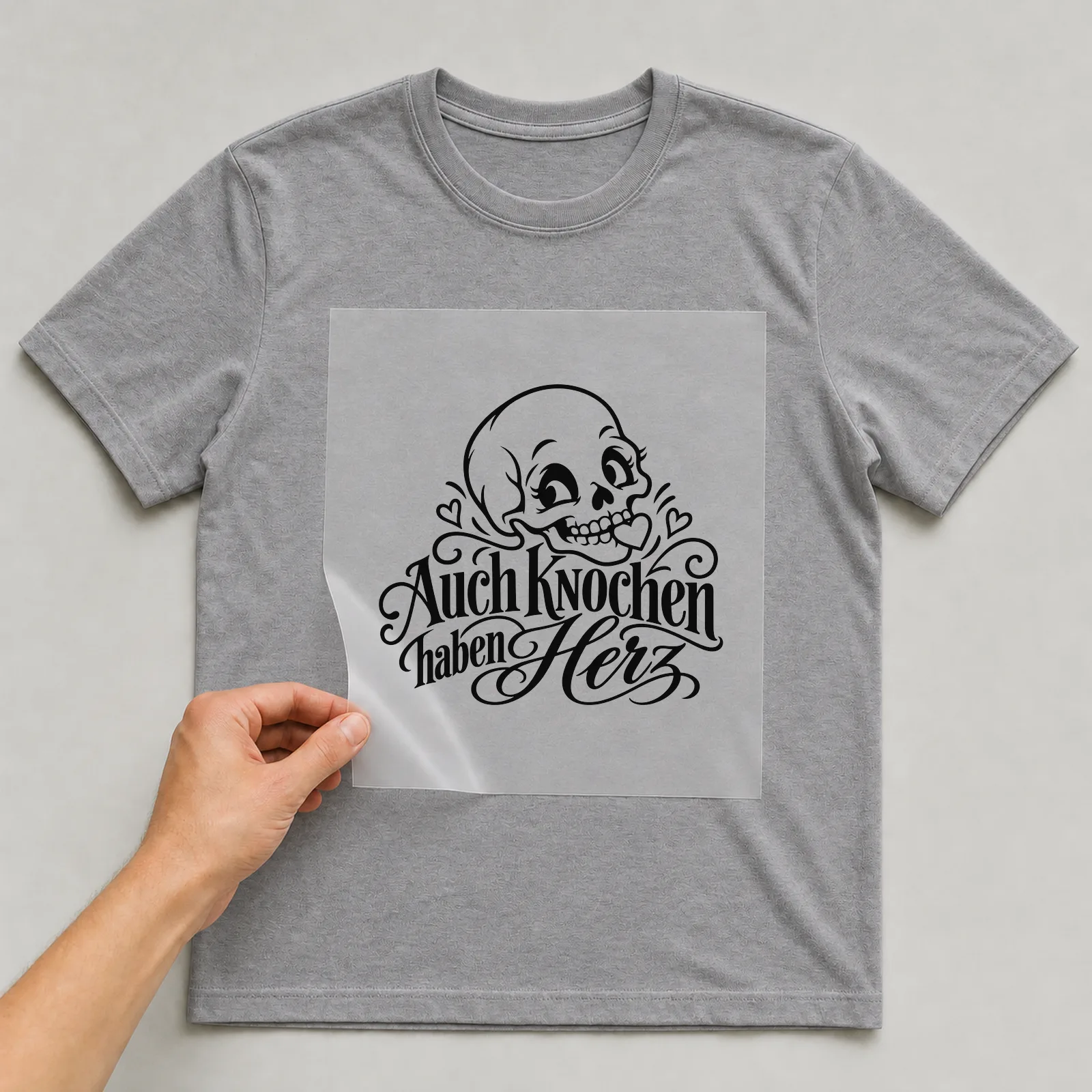 Bügelbild „Auch Knochen haben Herz“ auf grauem T-Shirt, Folie wird aufgelegt