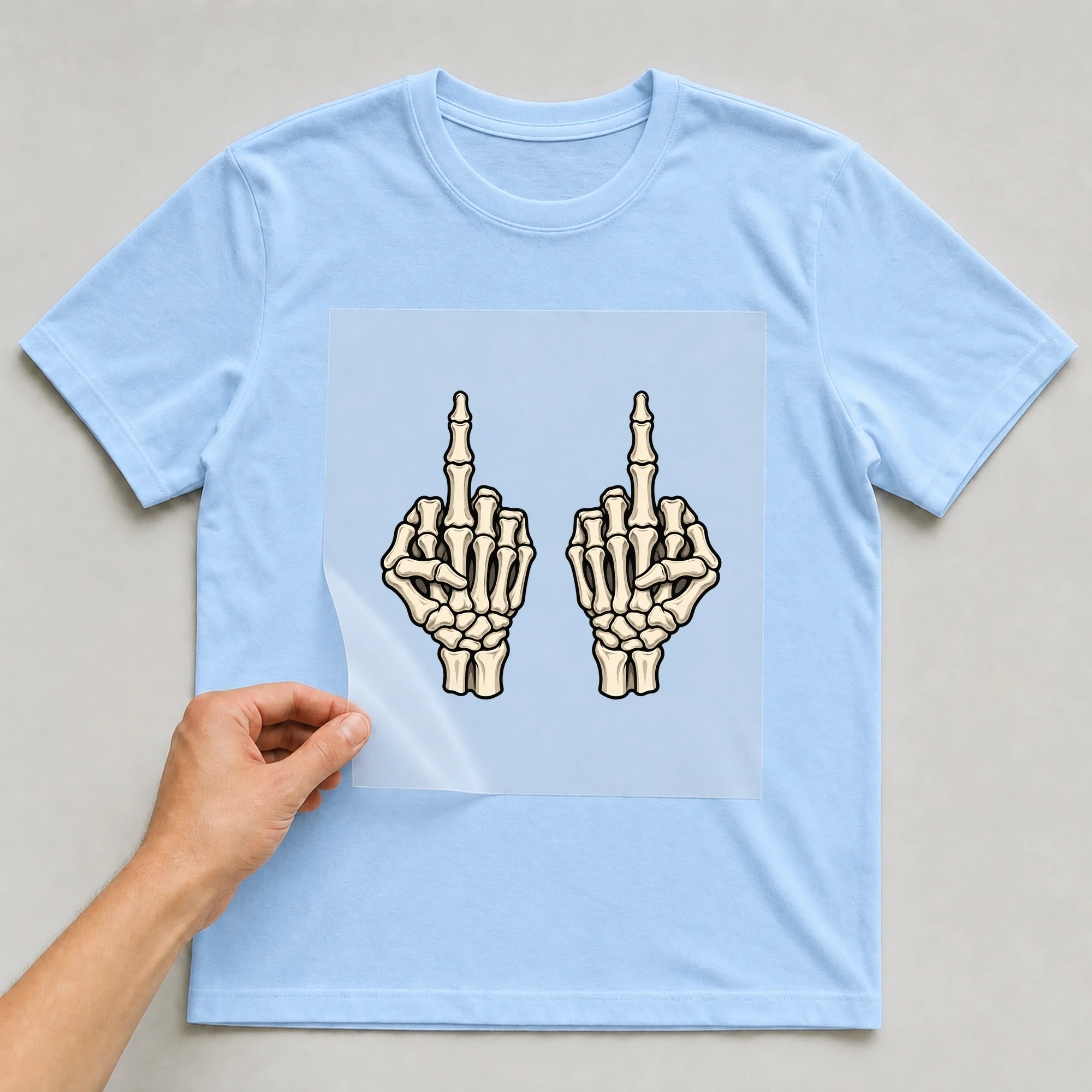 Bügelbild „Skelett Mittelfinger“ auf babyblauem T-Shirt, Folie wird aufgelegt