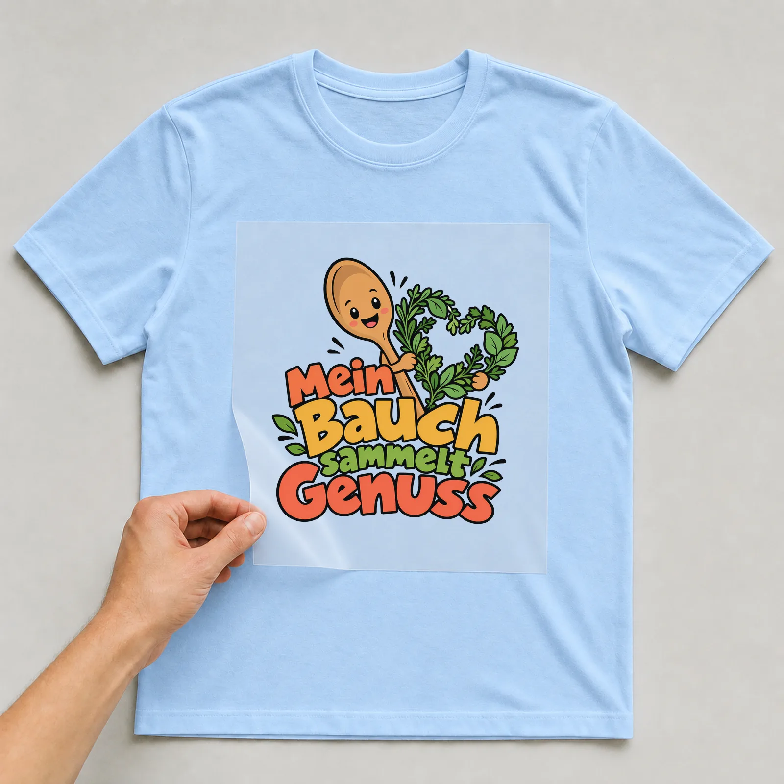 Bügelbild „Mein Bauch sammelt Genuss“ auf hellblauem T-Shirt, Folie wird aufgelegt
